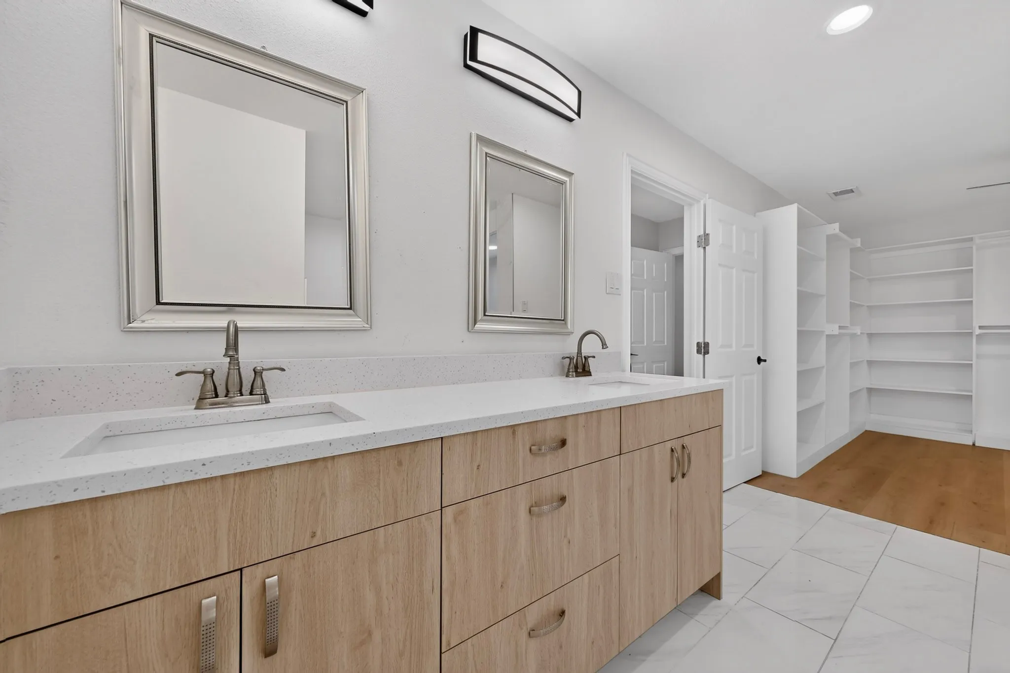 Dual vanity with light wood-finish cabinetry and white countertops, featuring two framed mirrors and brushed nickel fixtures