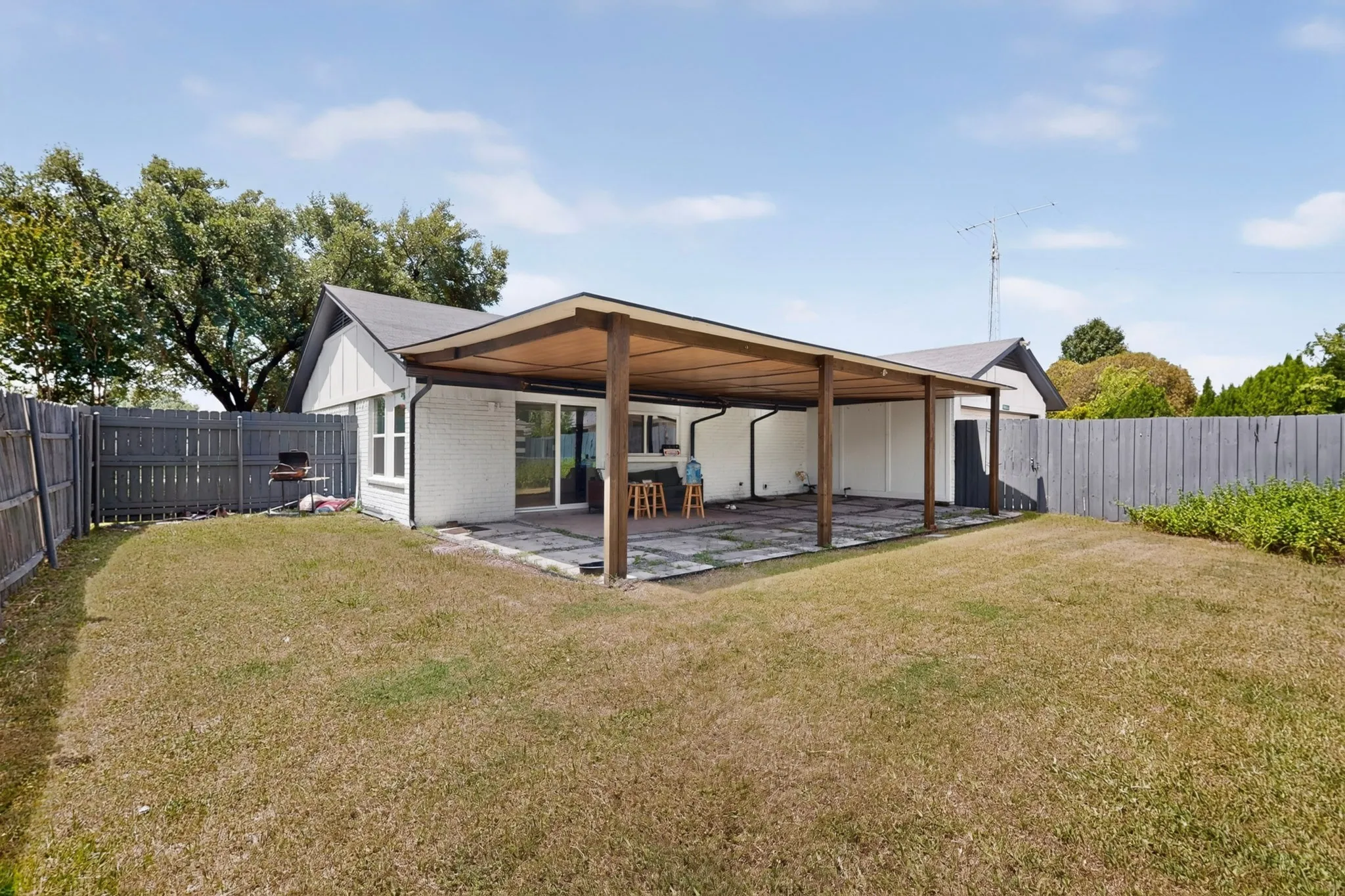 Spacious backyard featuring a covered patio with wood support beams, a concrete patio floor, and a sliding glass door entry to the home