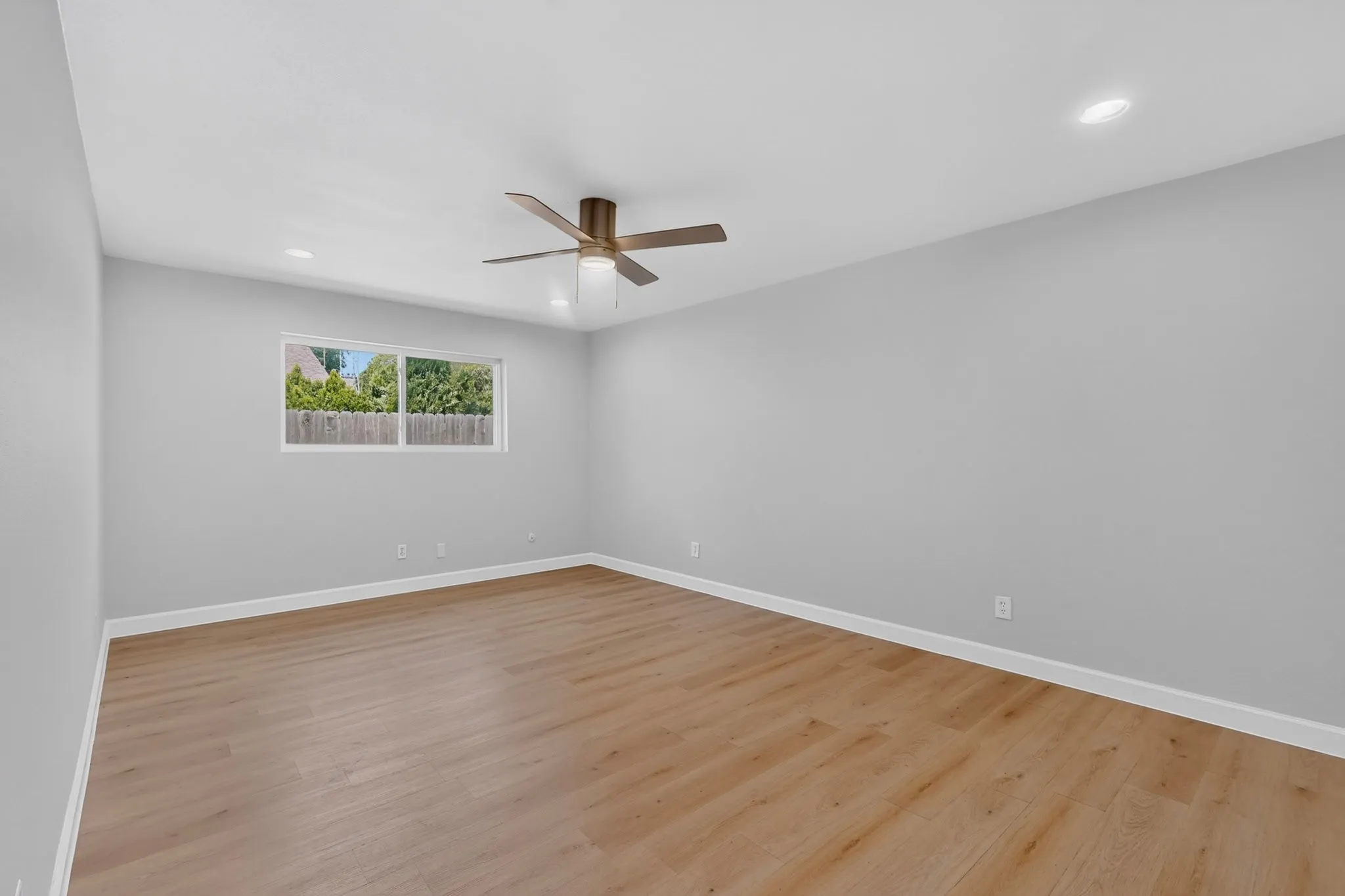 Spacious room featuring wood-finish flooring, light grey walls, and white baseboards