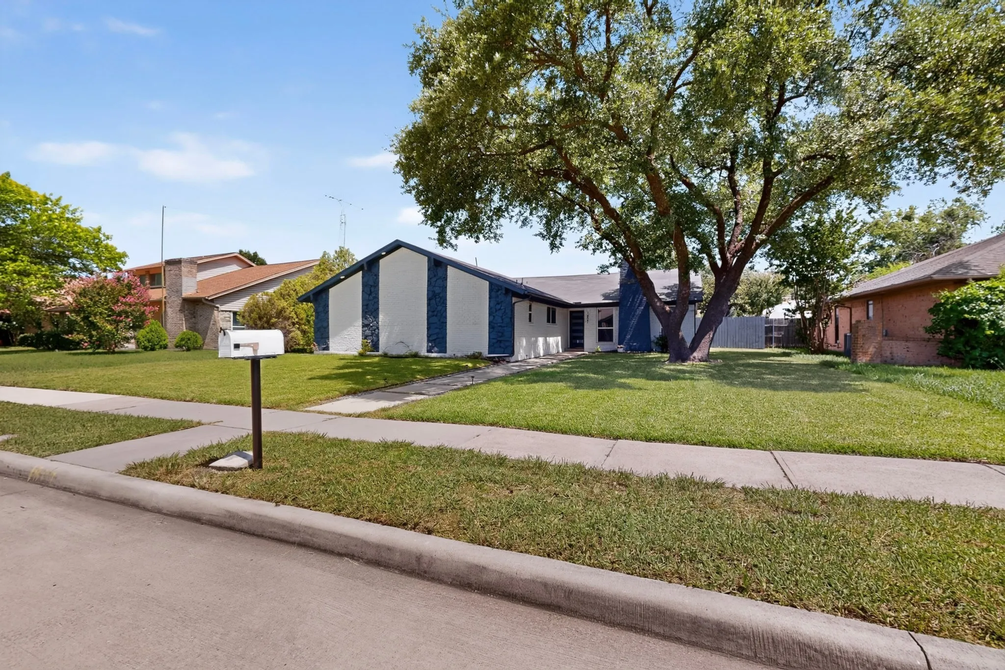 Single-story residence featuring a prominent mature tree, manicured lawn, and a sidewalk entrance