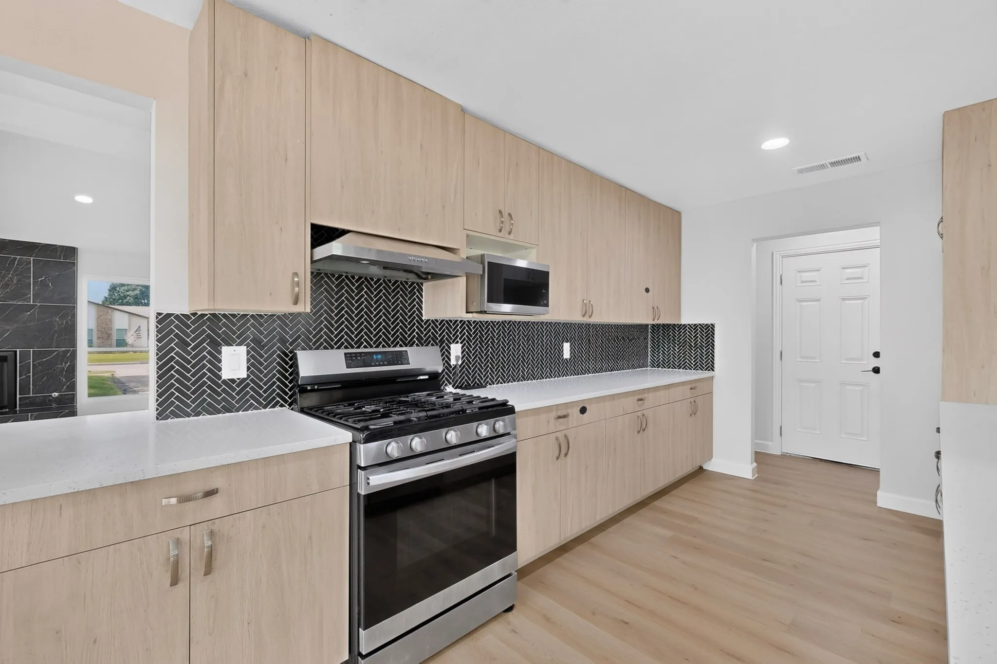 Kitchen featuring light wood-finish cabinetry, white countertops, and a black herringbone tile backsplash