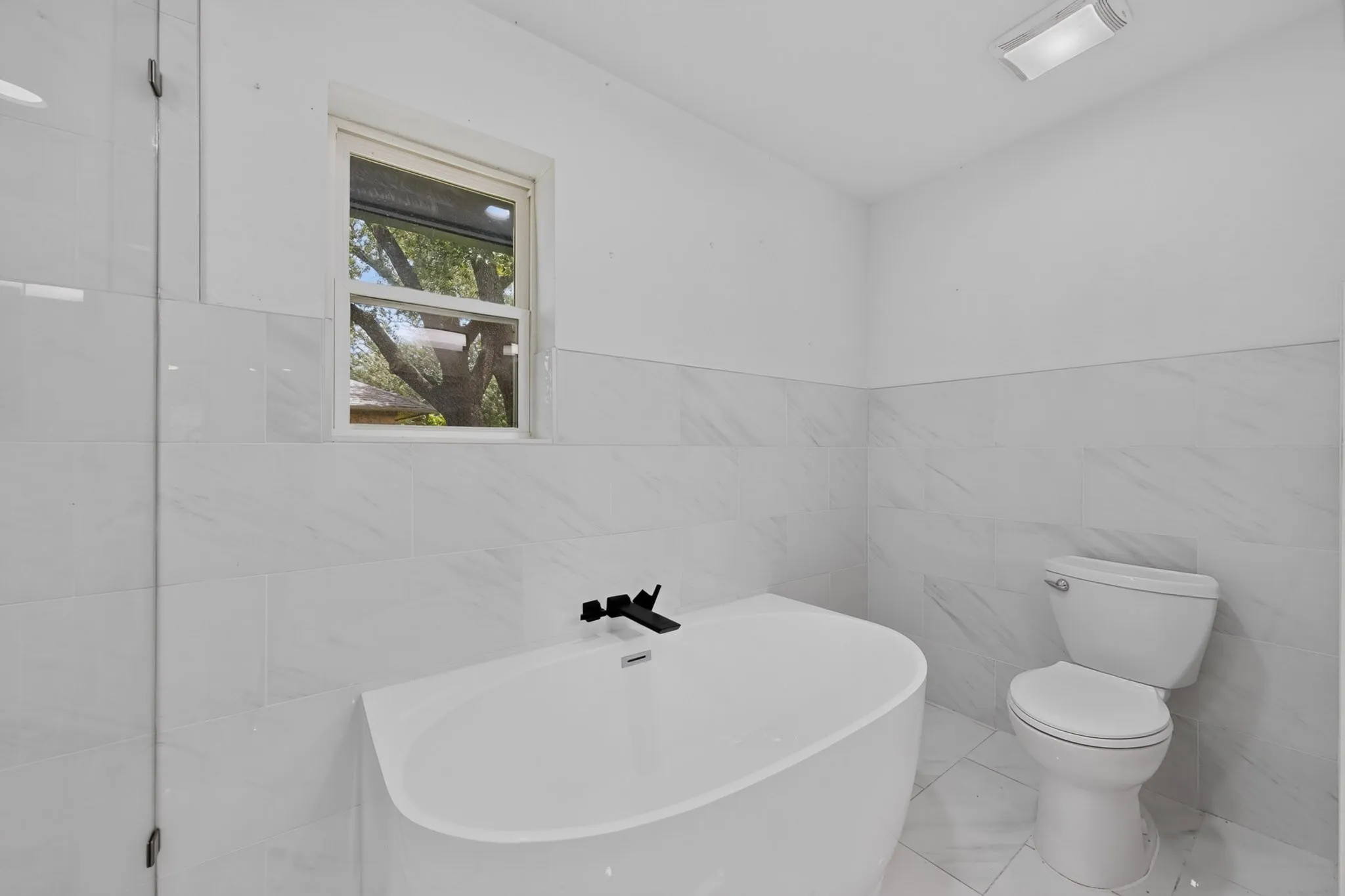 Bathroom featuring a freestanding soaking tub with matte black fixtures, a white toilet, and white tile flooring