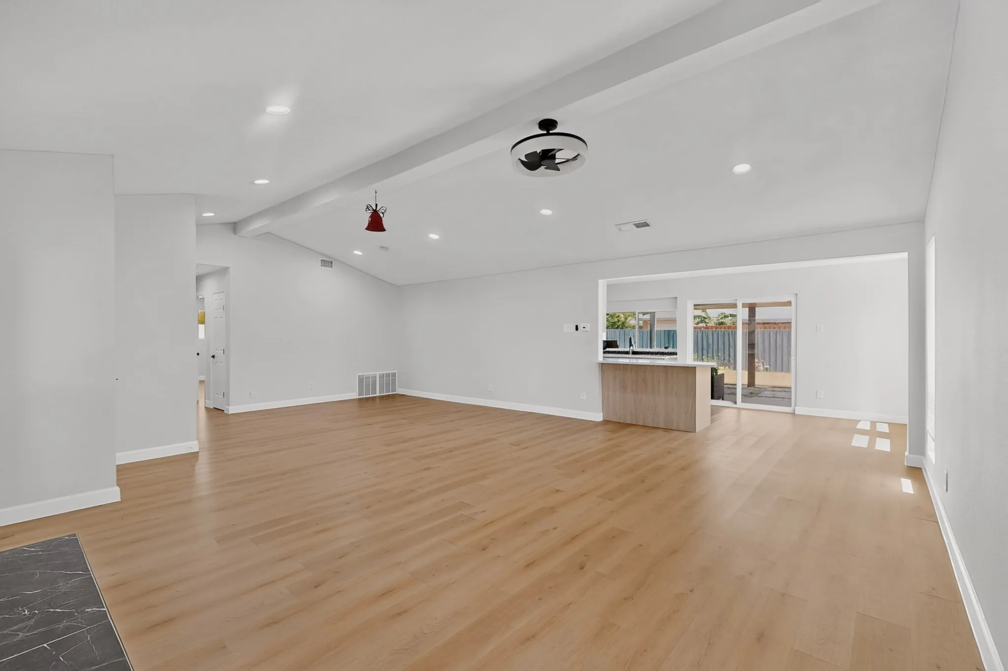 Spacious room featuring wood-finish flooring, vaulted ceilings with exposed beams, recessed lighting, and a modern ceiling fan