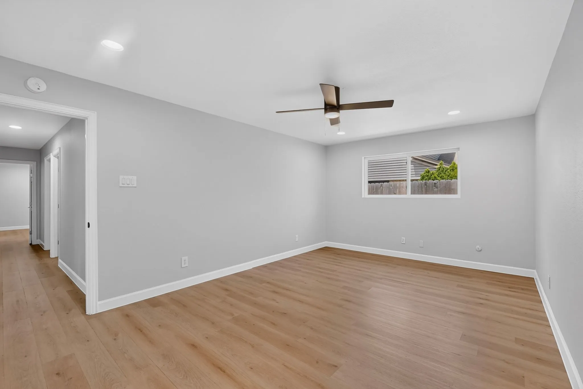 Spacious room featuring wood-finish flooring, light grey walls, white trim, and a contemporary ceiling fan