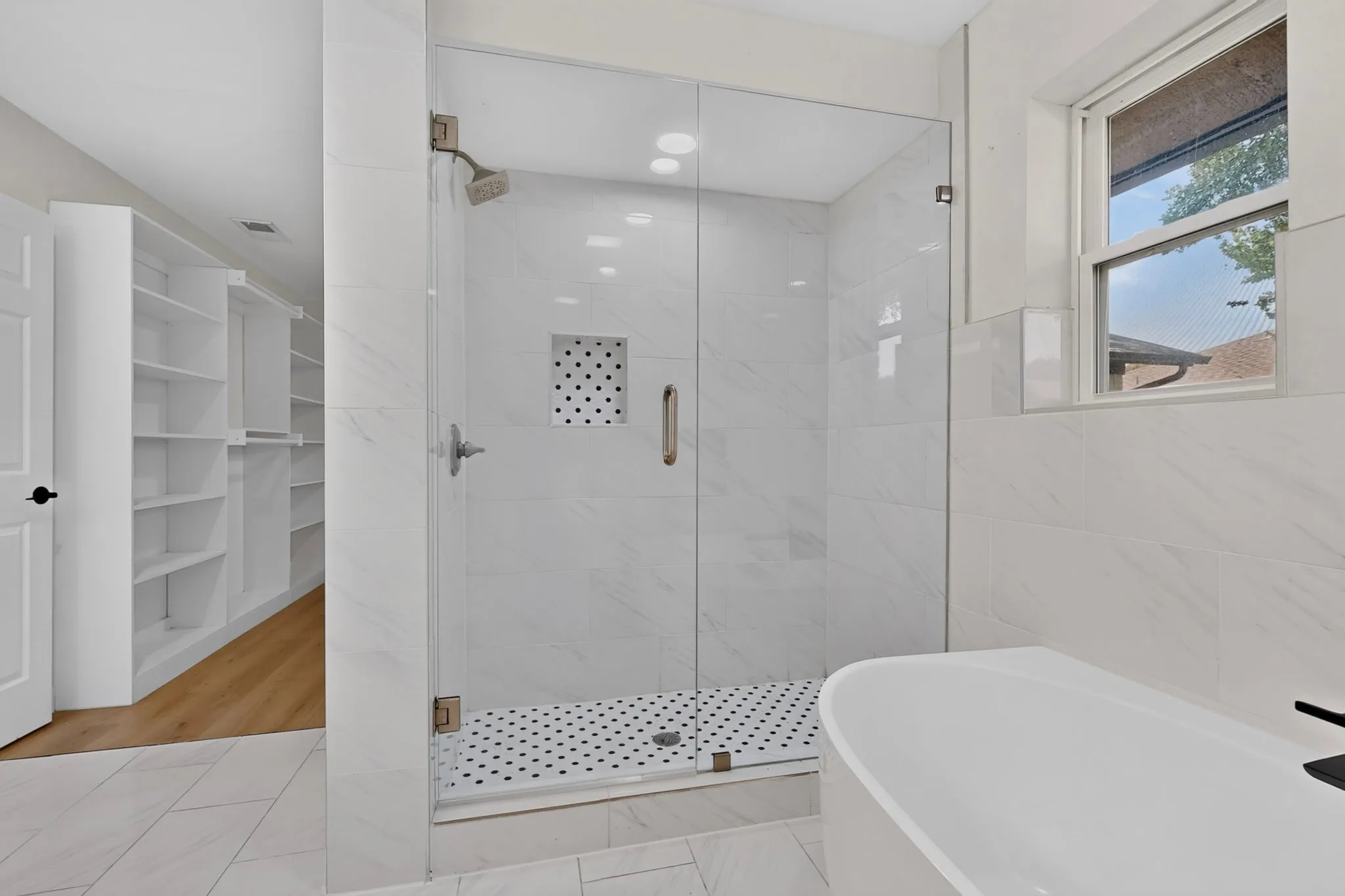 Glass-enclosed shower with white tiled walls and black-and-white mosaic floor