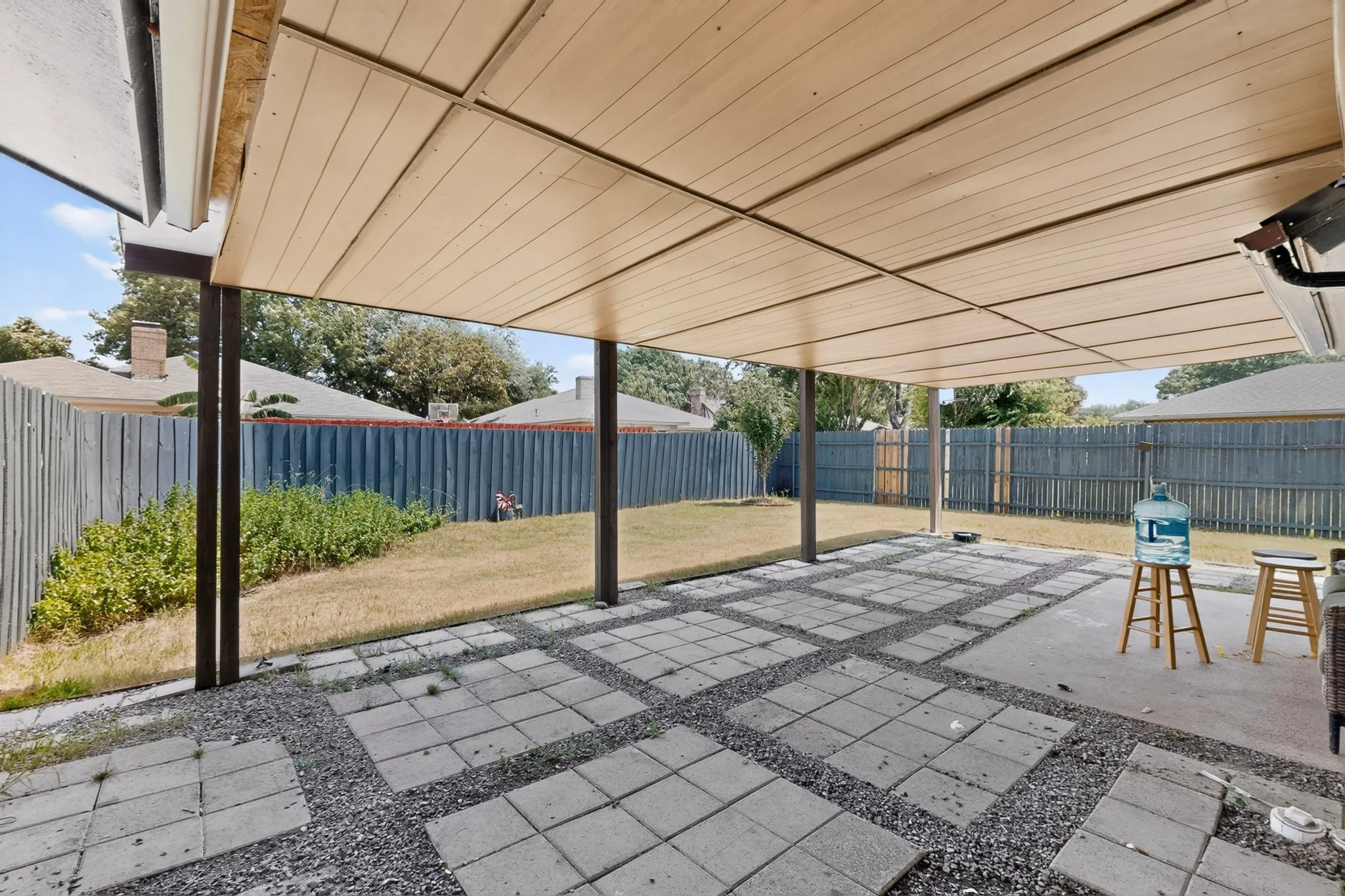 Expansive covered patio featuring a wood-finish ceiling, dark support beams, and a concrete and gravel paver surface