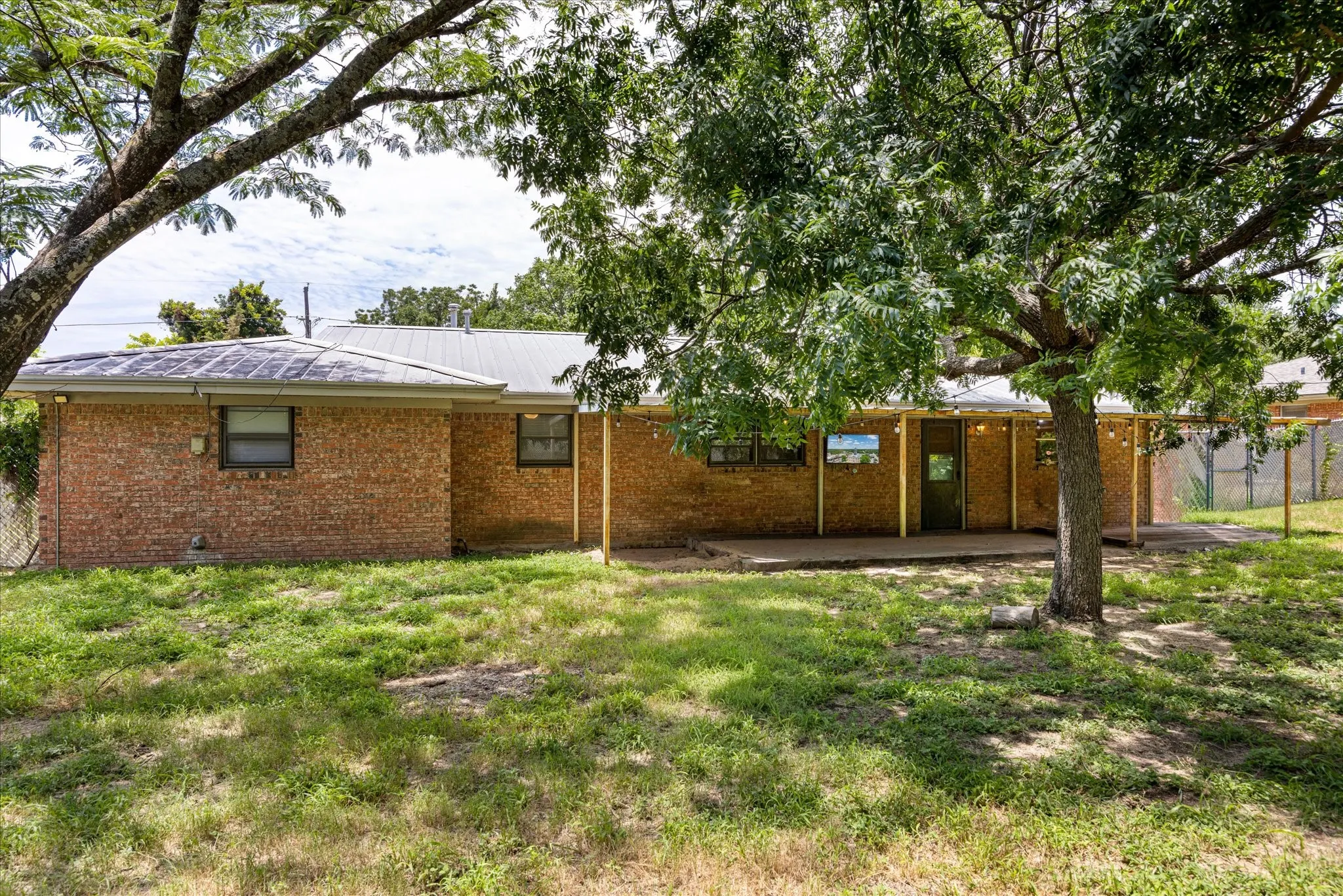 Rear exterior featuring a brick facade, metal roof, and a covered patio area