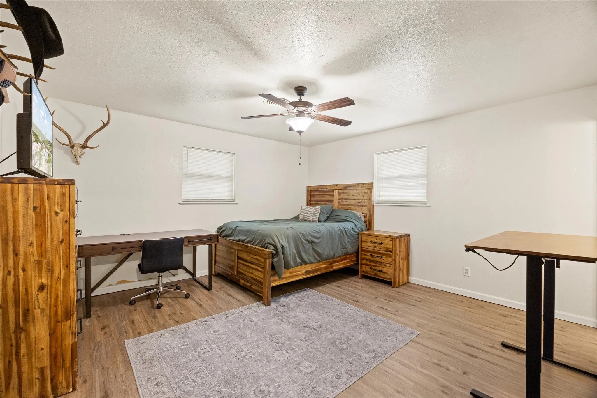 Primary room featuring wood-finish flooring, two windows with blinds, a ceiling fan with integrated lighting, and white walls