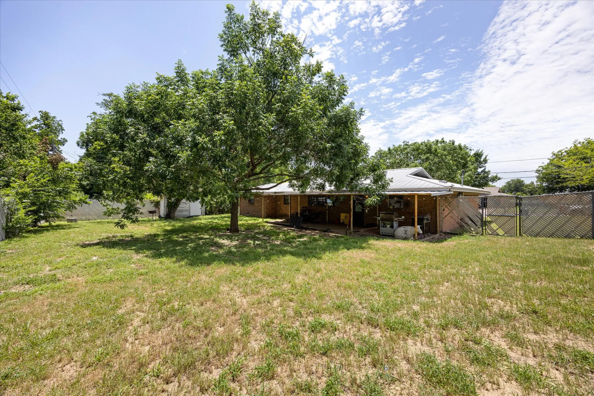 Expansive backyard featuring a large tree providing shade, a covered patio area, and perimeter fencing