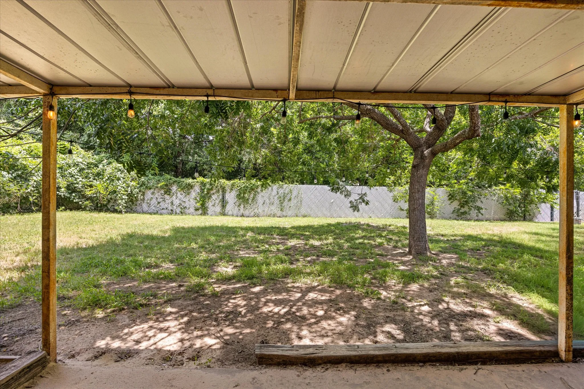 Covered patio featuring a concrete floor, wooden support beams, and string lighting