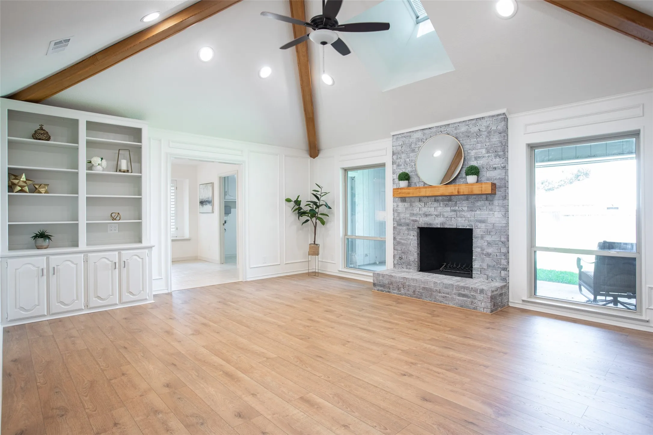 Freshly updated living room featuring new flooring, freshly painted walls and ceiling, a new ceiling fan, whitewashed fireplace, and built-in shelving.