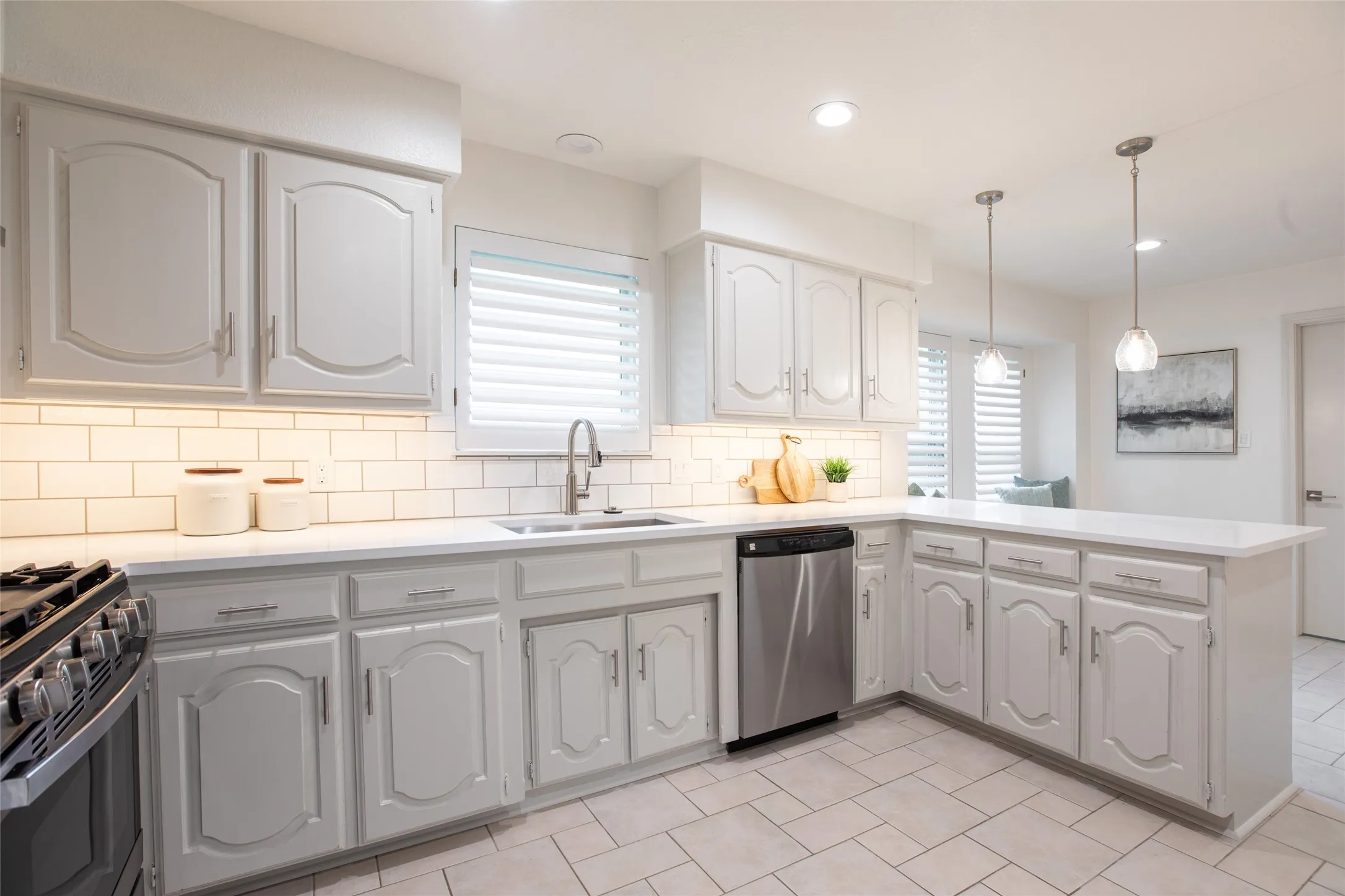 Updated kitchen featuring freshly painted cabinetry, white quartz countertops, new backsplash, new gas range, updated lighting, new cabinet hardware, and new faucet.