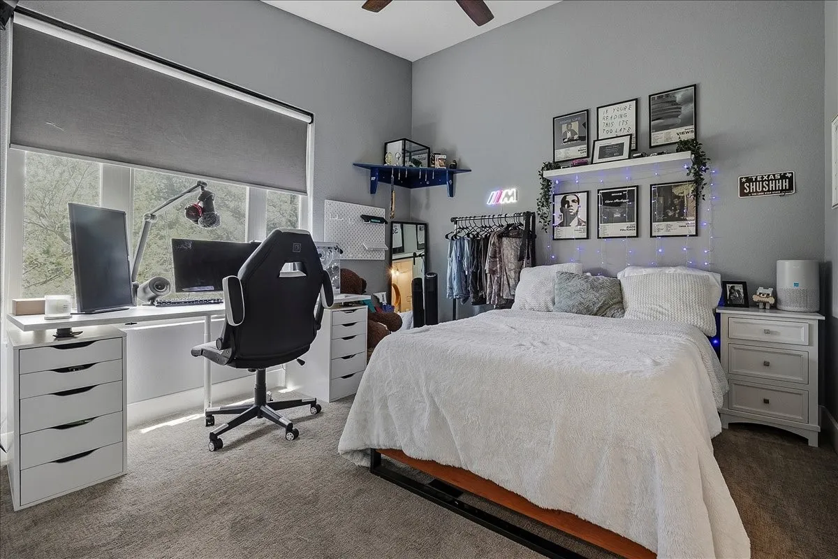 Bedroom featuring a large window with a roller shade, light gray walls, and carpet flooring