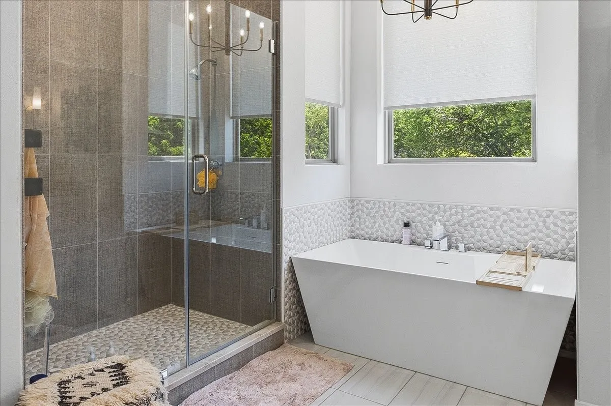 Freestanding soaking tub with a patterned tile surround, accompanied by a glass-enclosed shower featuring large format wall tile and pebble-style flooring