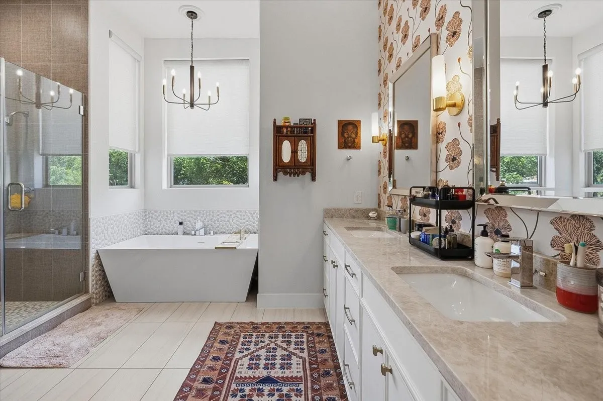 Freestanding soaking tub with mosaic tile surround, dual vanity with undermount sinks and stone countertops, and a glass-enclosed shower with tiled walls