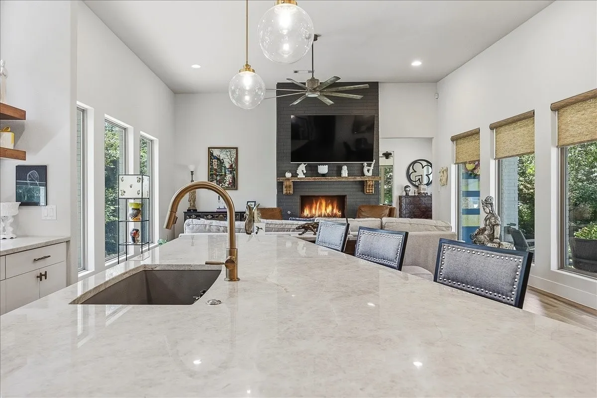 Spacious interior featuring a large kitchen island with an undermount sink and brass faucet, soaring ceilings, a modern fireplace with a dark tile surround, and expansive windows