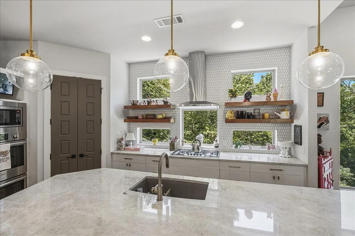 Kitchen featuring a large central island with an undermount sink and a satin nickel faucet, light-toned cabinetry, stainless steel appliances, and a tiled backsplash