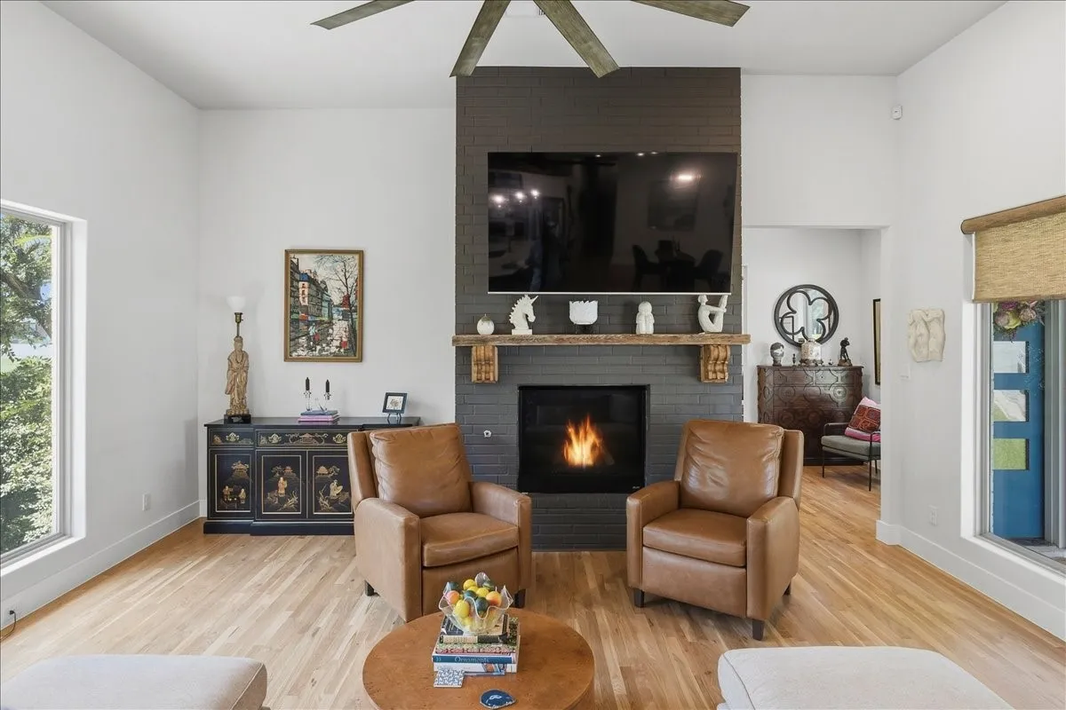 Vaulted ceiling living area featuring a prominent dark brick fireplace with a rustic wood mantel, an integrated television, and light wood-finish flooring