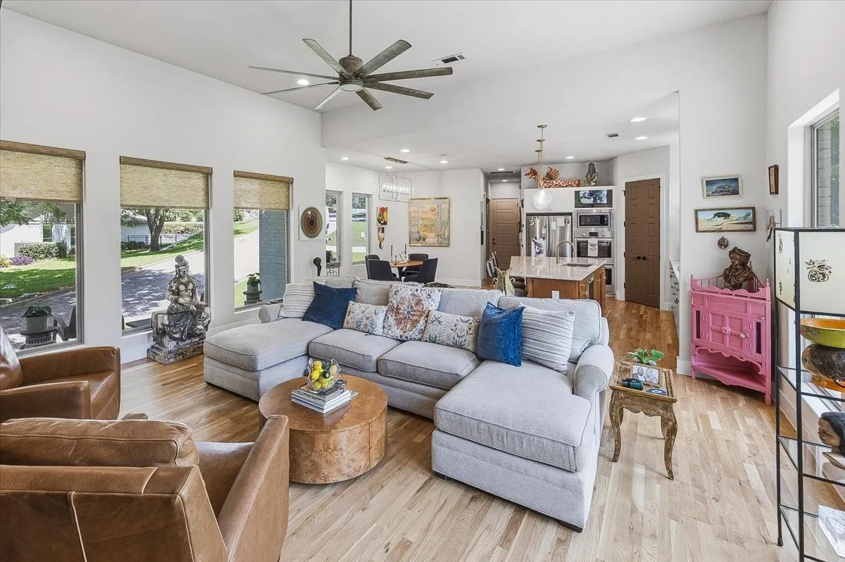 Spacious living area featuring high ceilings, recessed lighting, wood-finish flooring, a large ceiling fan, and multiple windows with roller shades