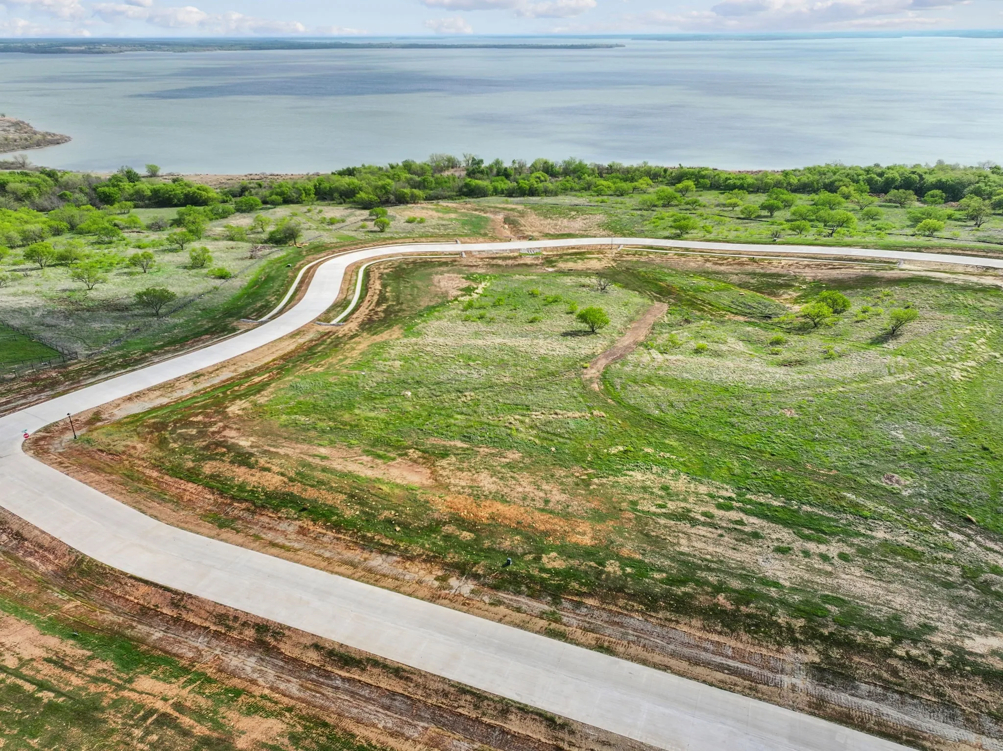 Expansive land parcel featuring paved roads, lush green grass, scattered trees, and direct frontage on a significant body of water