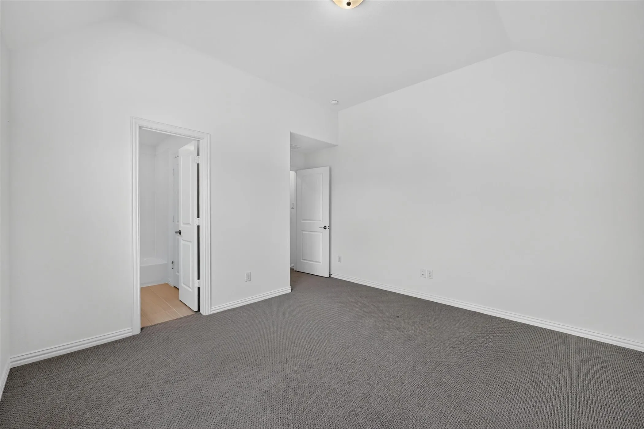 Spacious room featuring vaulted ceilings, a neutral color palette, and gray carpeting