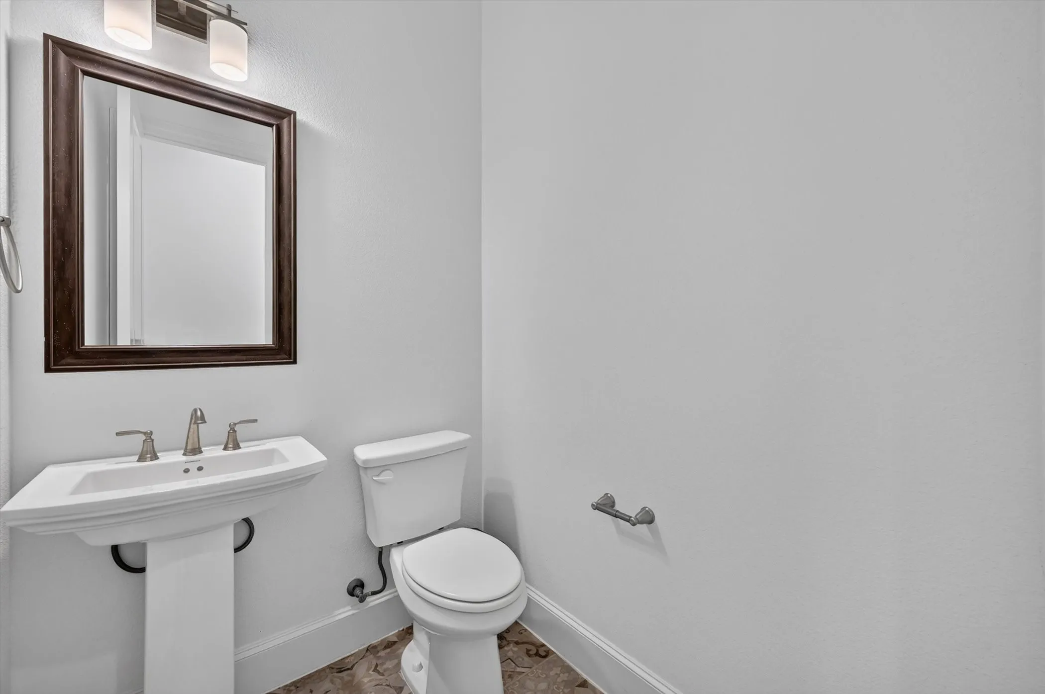 Pedestal sink with brushed nickel faucet, framed mirror, and wall-mounted lighting