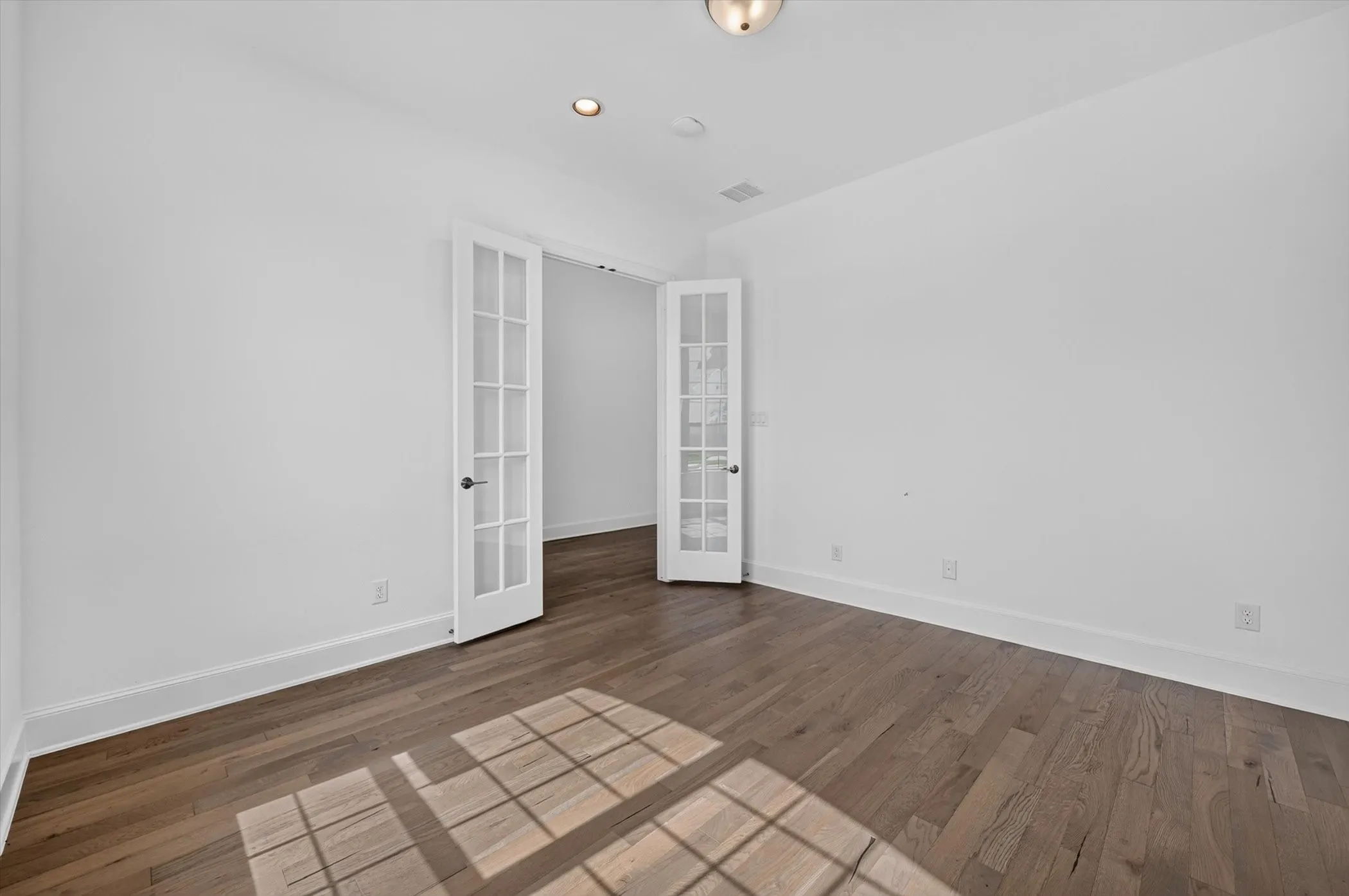 Room featuring wood-finish flooring, white walls, and bright overhead lighting