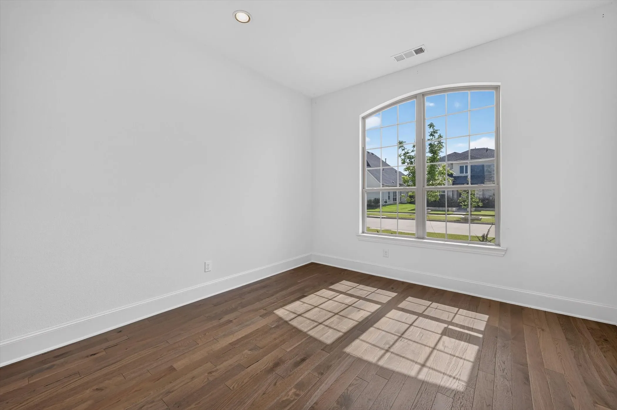 Room featuring an arched window with grid-patterned panes, wood-finish flooring, and recessed ceiling lighting