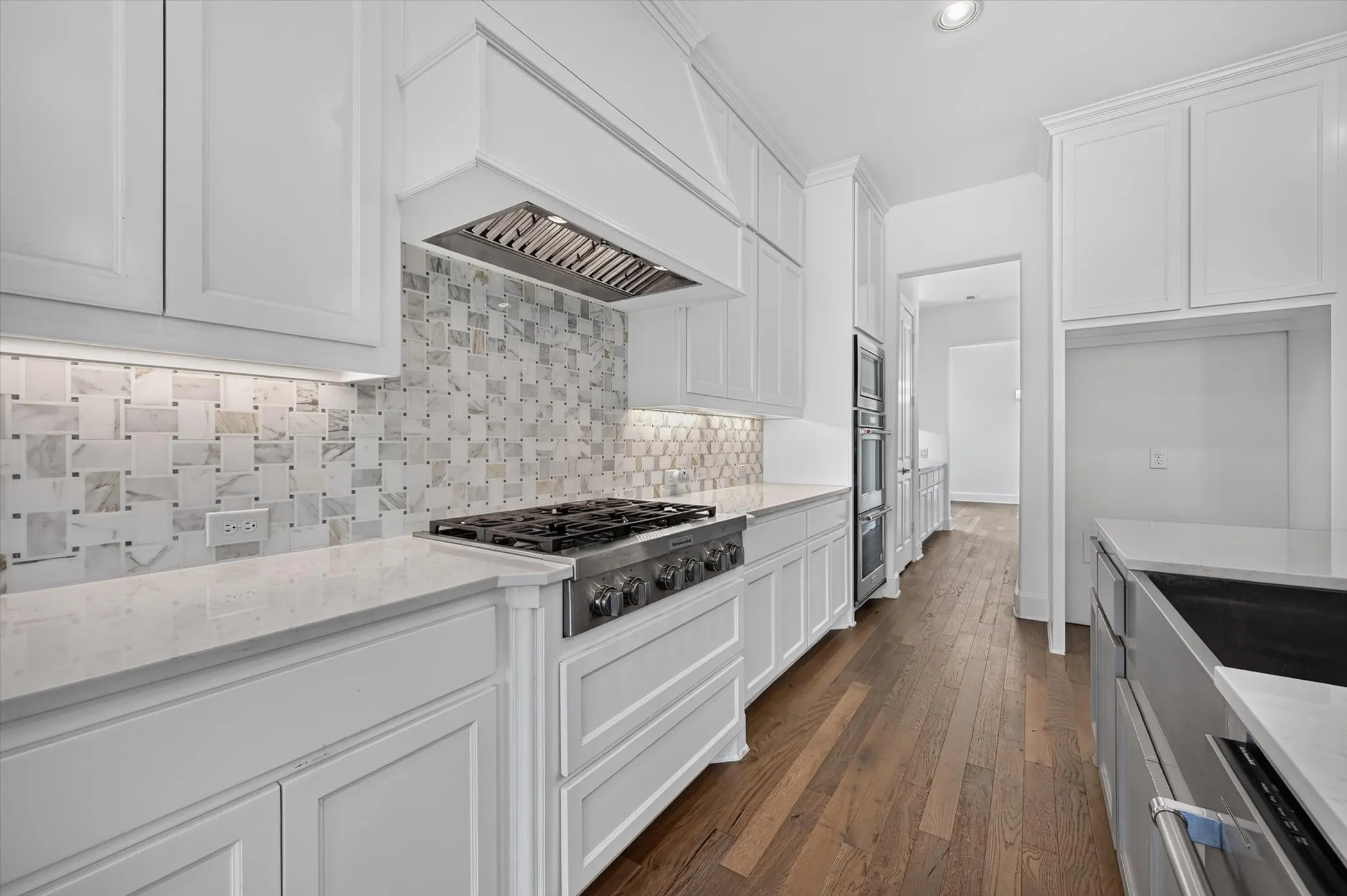 Gourmet kitchen featuring a six-burner gas range, custom range hood, double wall ovens, and white shaker cabinetry