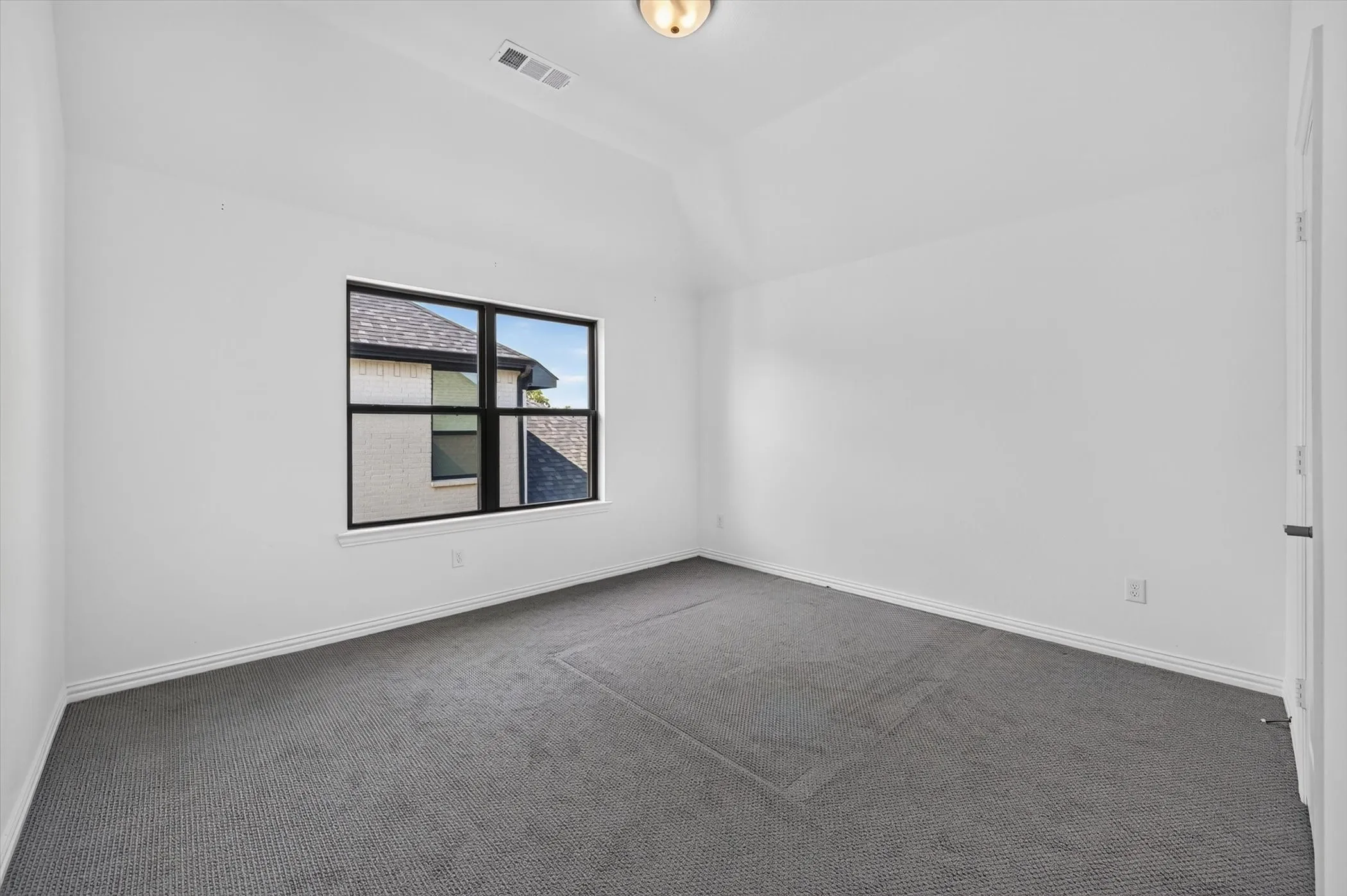 Carpeted room featuring a single window with black framing, white walls, vaulted ceiling, and recessed lighting