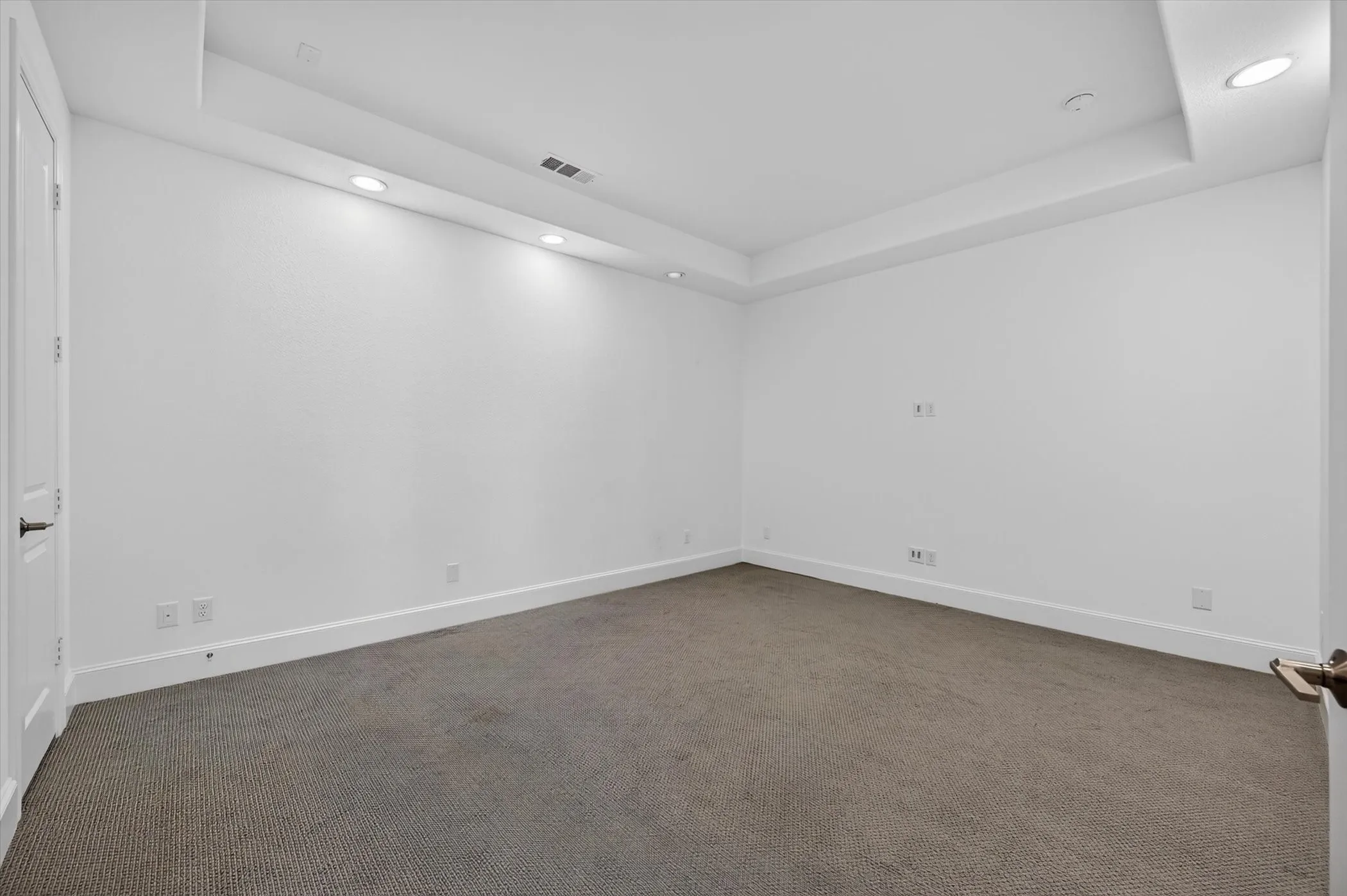 Recessed lighting illuminates a spacious room featuring a tray ceiling and carpet flooring