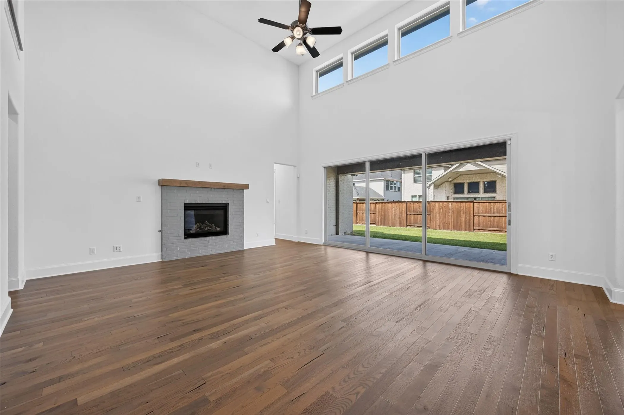 Spacious living area featuring high vaulted ceilings, wood-finish flooring, and a fireplace with a light gray tile surround and wood mantel