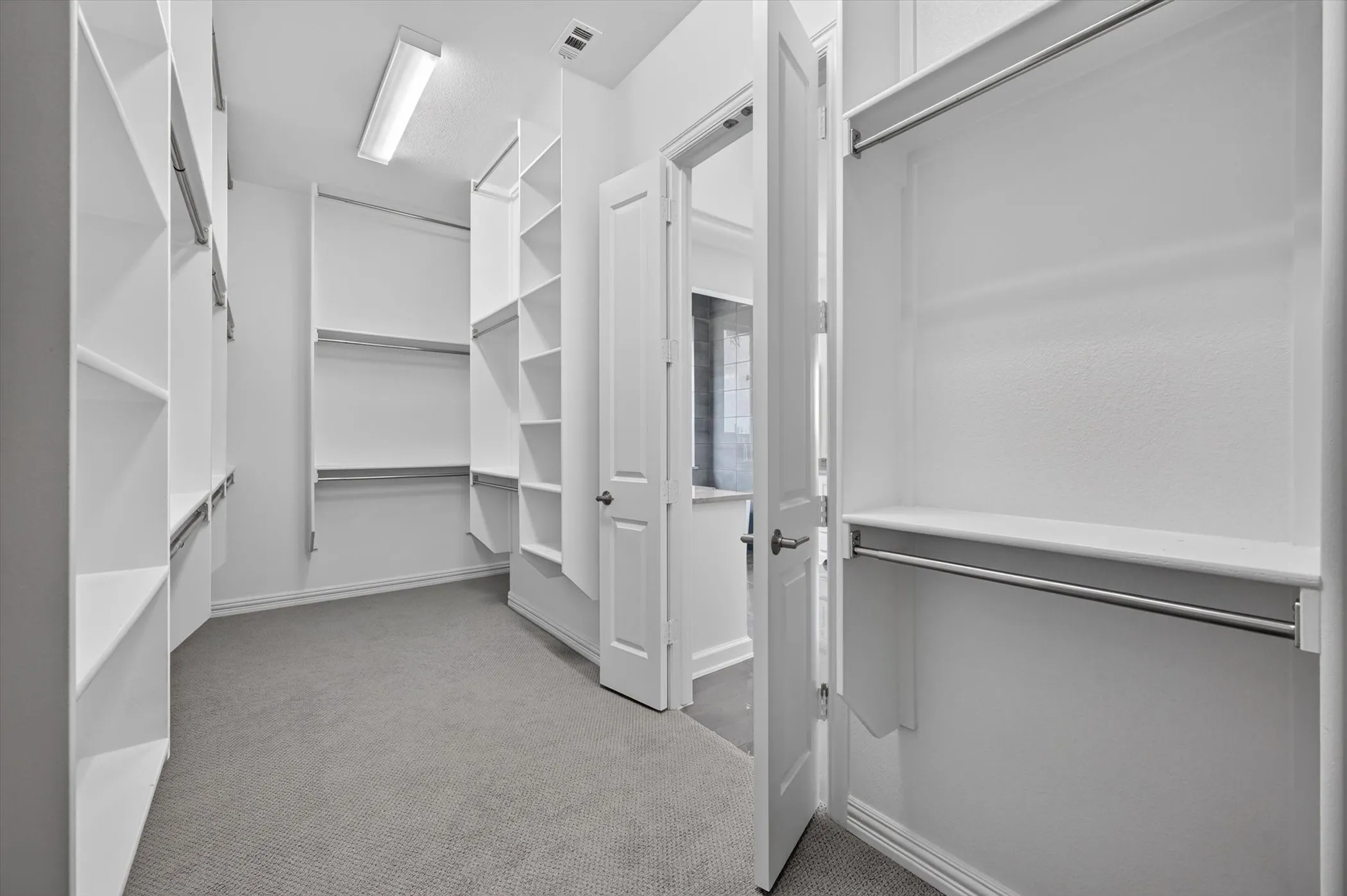 Spacious walk-in closet featuring extensive built-in shelving, multiple hanging rods, recessed lighting, and soft gray carpeting