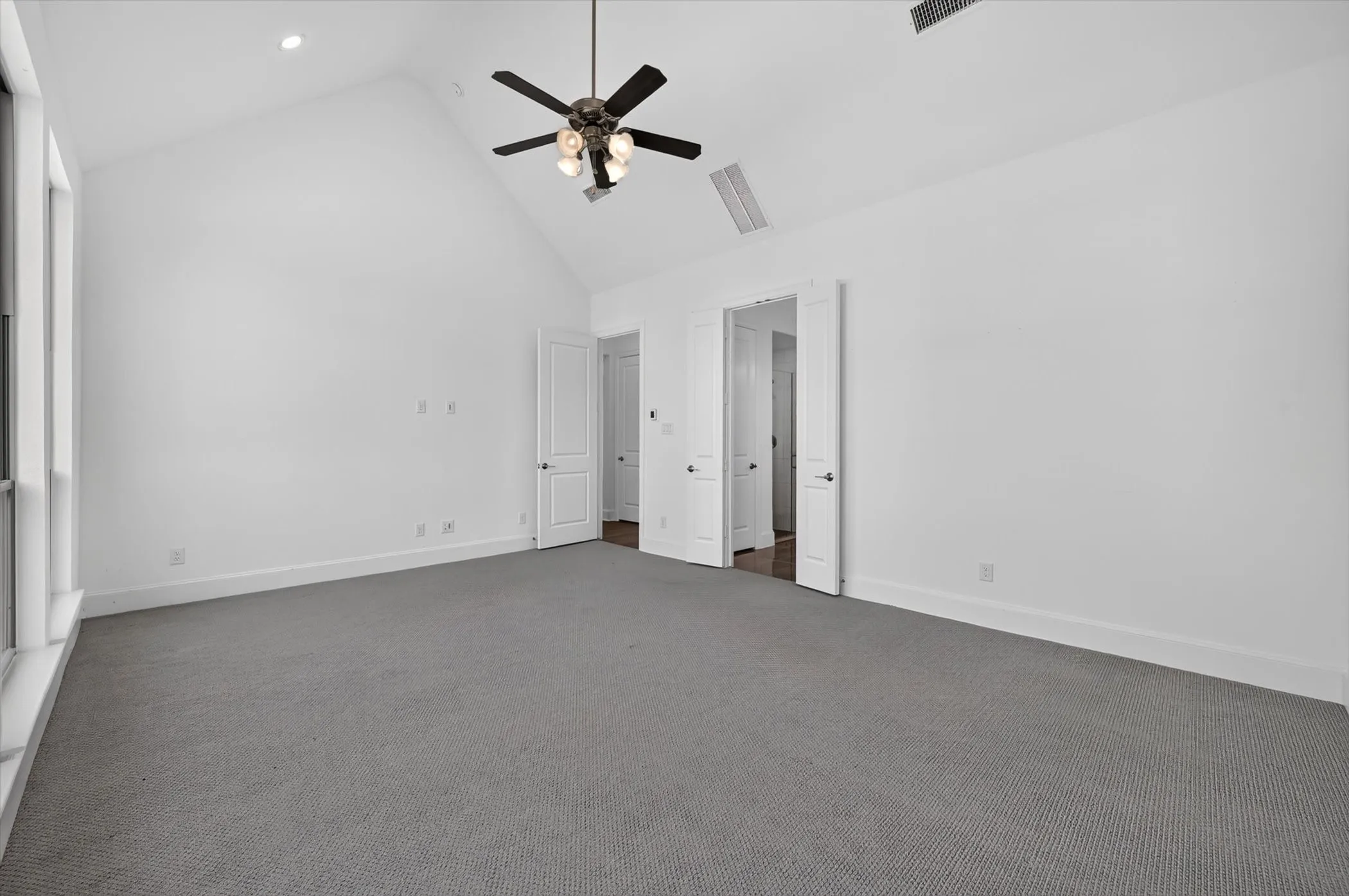 Spacious room featuring a vaulted ceiling with a ceiling fan, recessed lighting, white walls, gray carpeting, and multiple windows
