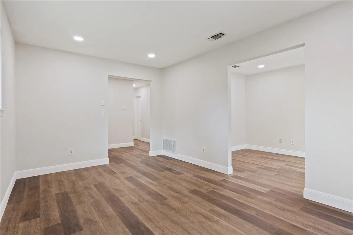 Spacious room featuring wood-finish flooring, recessed lighting, white baseboards, and neutral wall tones