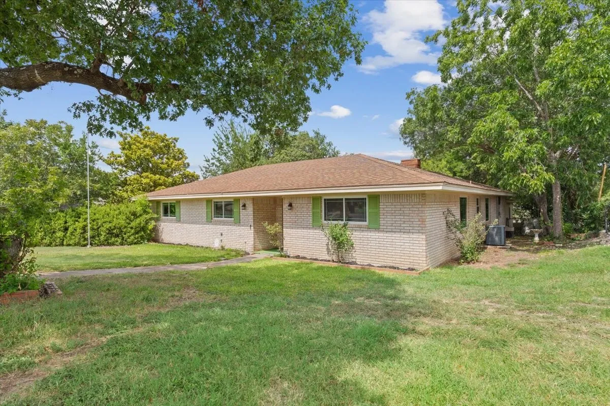Brick exterior featuring green shutters, a brown shingle roof, and established landscaping