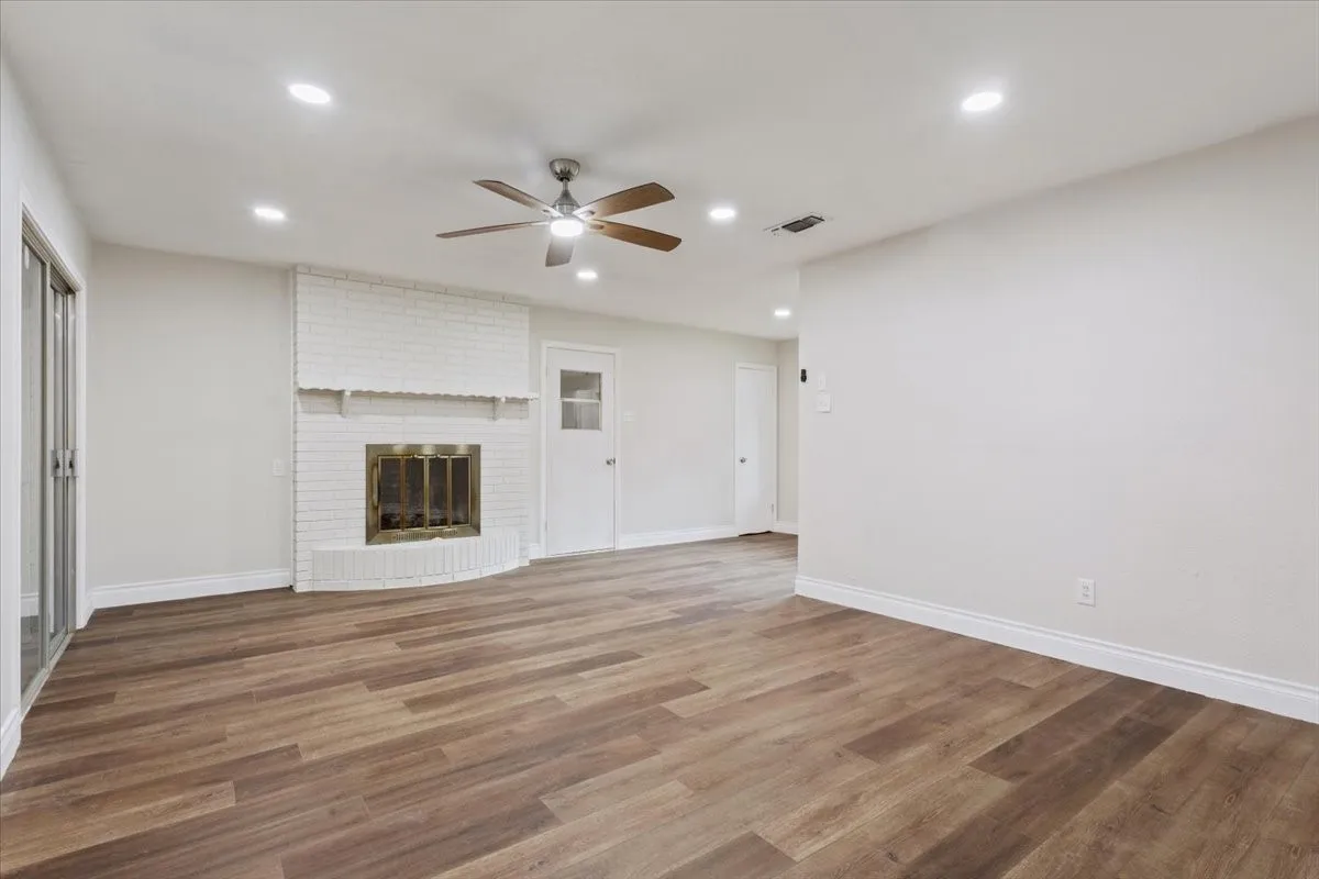 Spacious interior featuring wood-finish flooring, a white brick fireplace with a brass-toned firebox, recessed lighting, and a ceiling fan