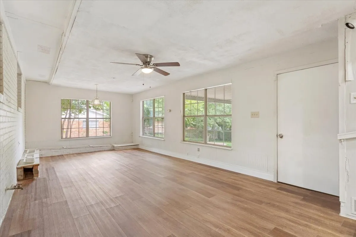 Spacious interior room featuring wood-finish flooring, white painted brick wall, and multiple windows