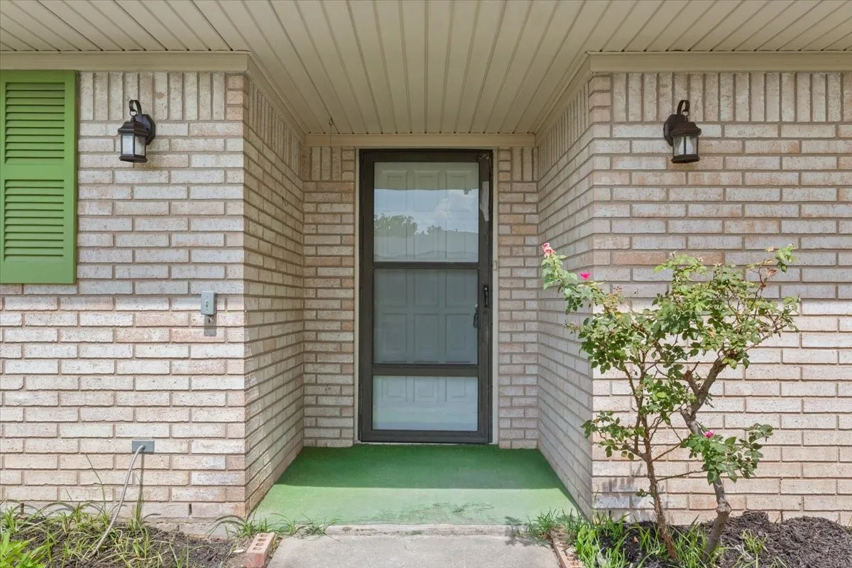 Brick exterior featuring a recessed entry, green louvered shutter, and twin black wall-mounted lanterns