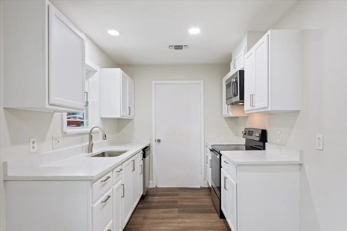 Bright kitchen featuring white cabinetry with silver hardware, white countertops, stainless steel sink with a gooseneck faucet, and wood-finish flooring