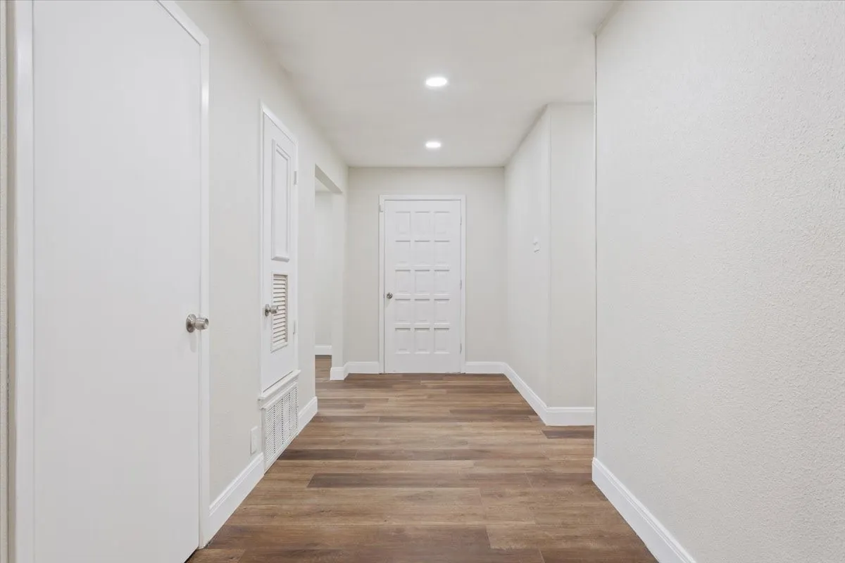 Hallway featuring wood-finish flooring, white baseboards, recessed lighting, and smooth white walls