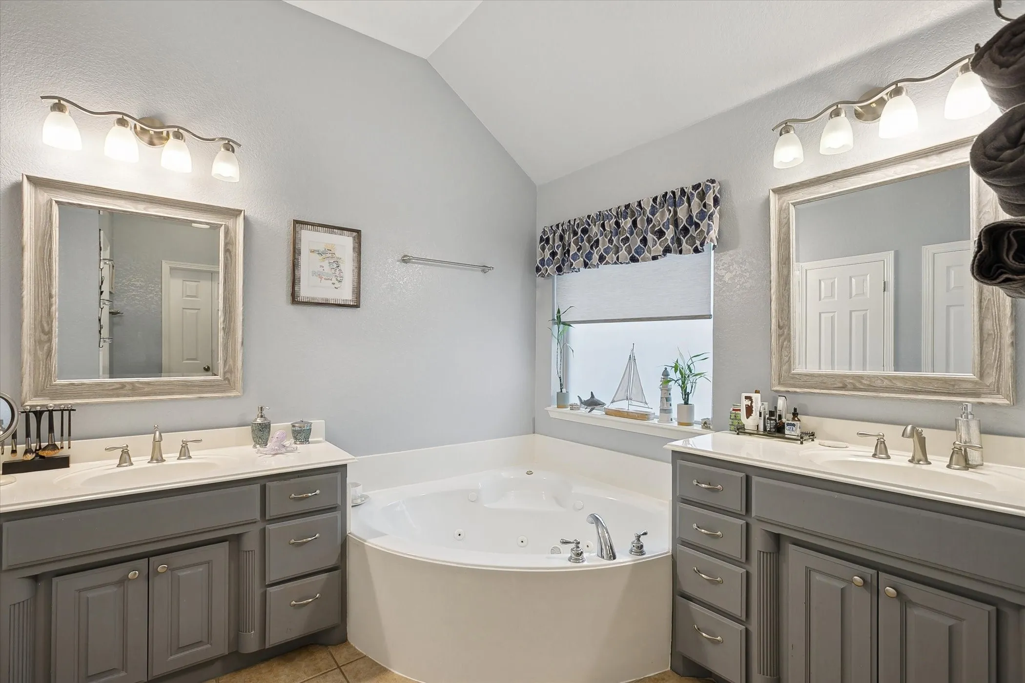 Primary bathroom with corner jetted tub featuring dual vanity sinks with light countertops and gray cabinetry