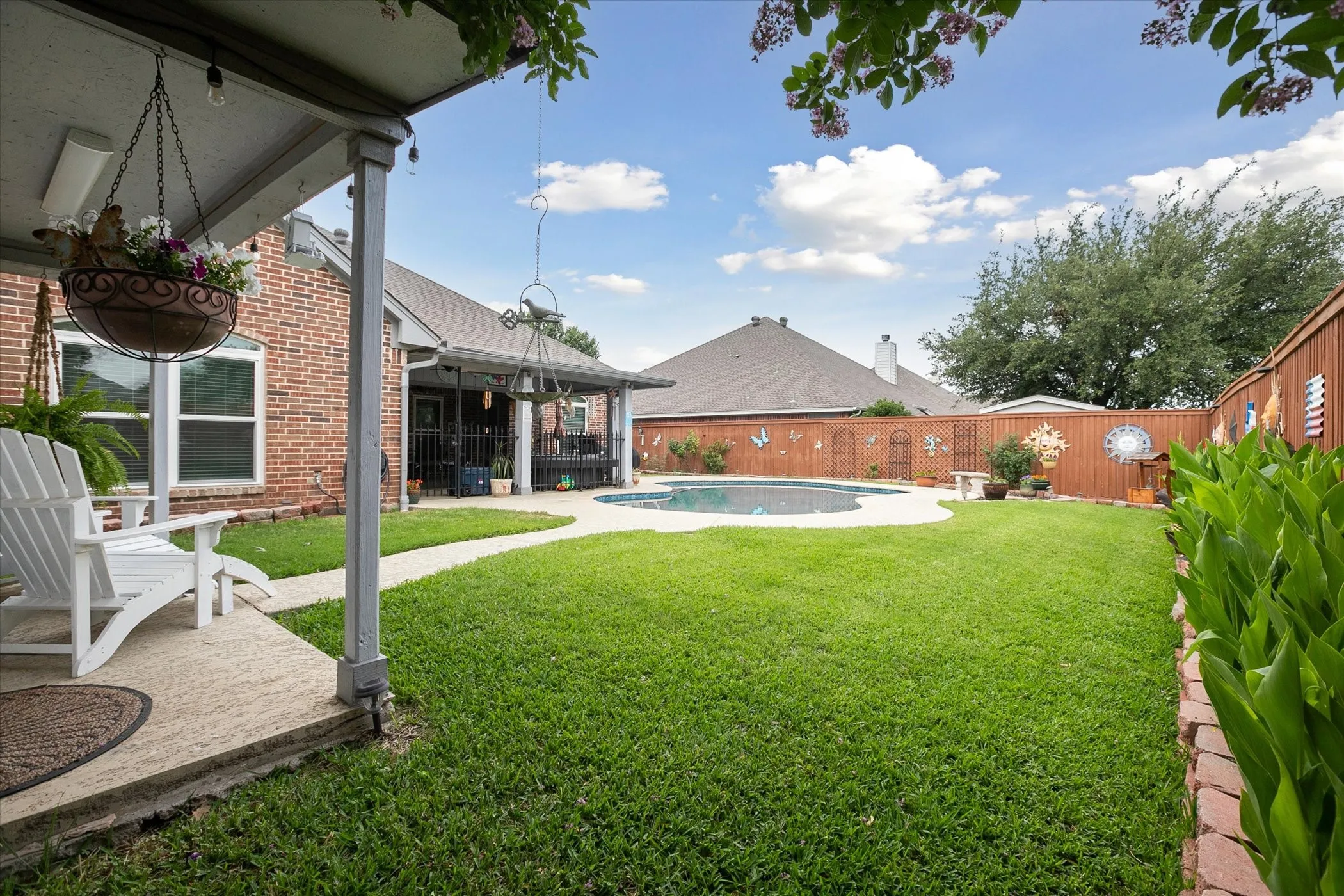 Expansive backyard featuring a curved in-ground pool with surrounding concrete decking, a covered patio, and a privacy fence