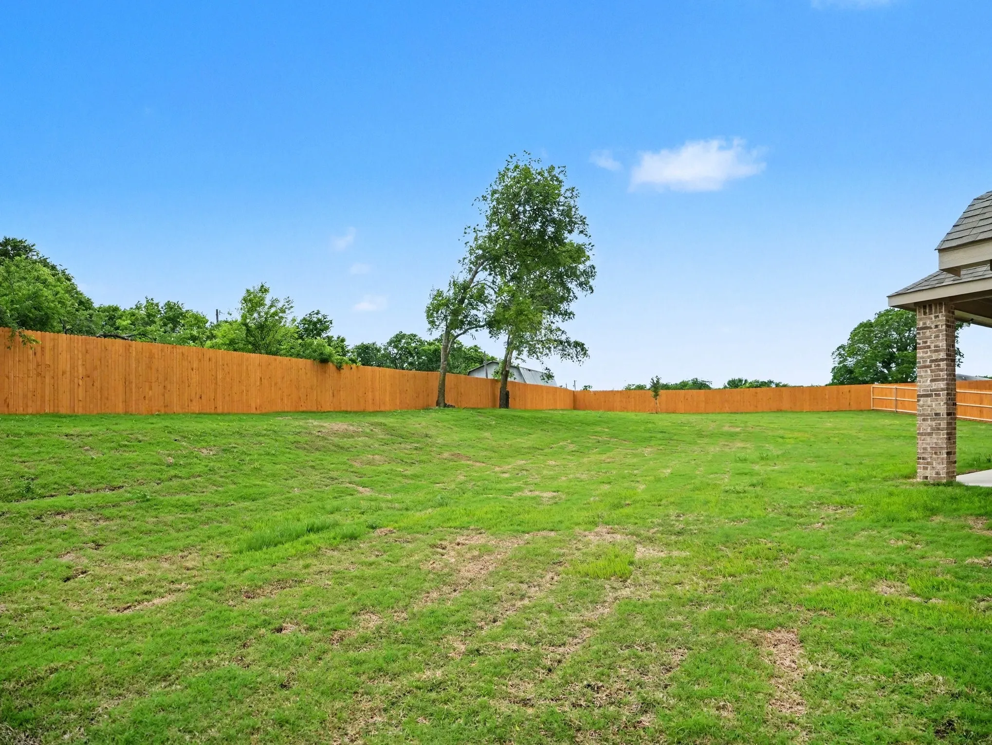 Expansive backyard featuring a lush green lawn, full wood privacy fence, and mature trees
