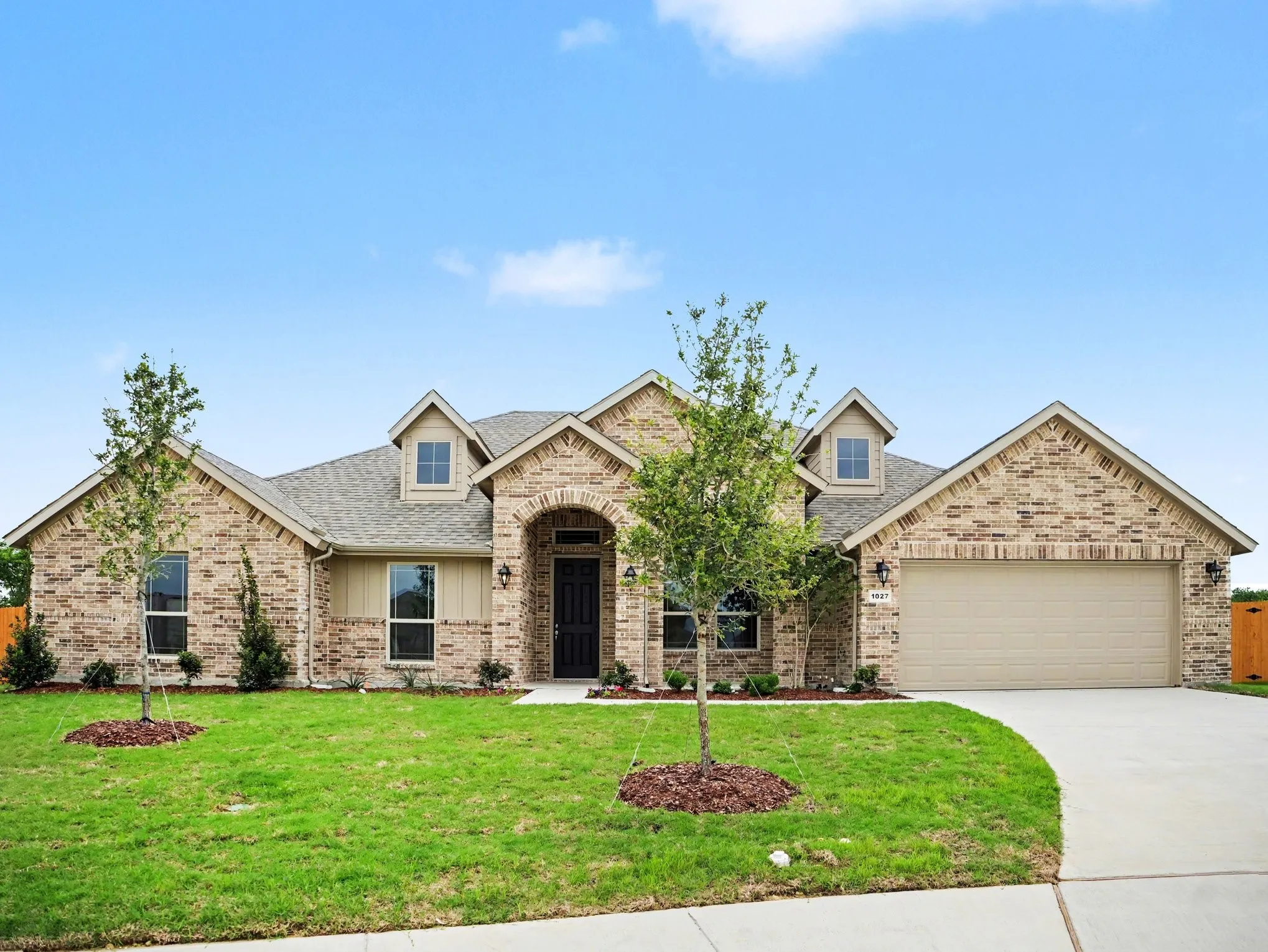 Brick and siding exterior featuring an arched entryway, dormer windows, a two-car garage, and established landscaping