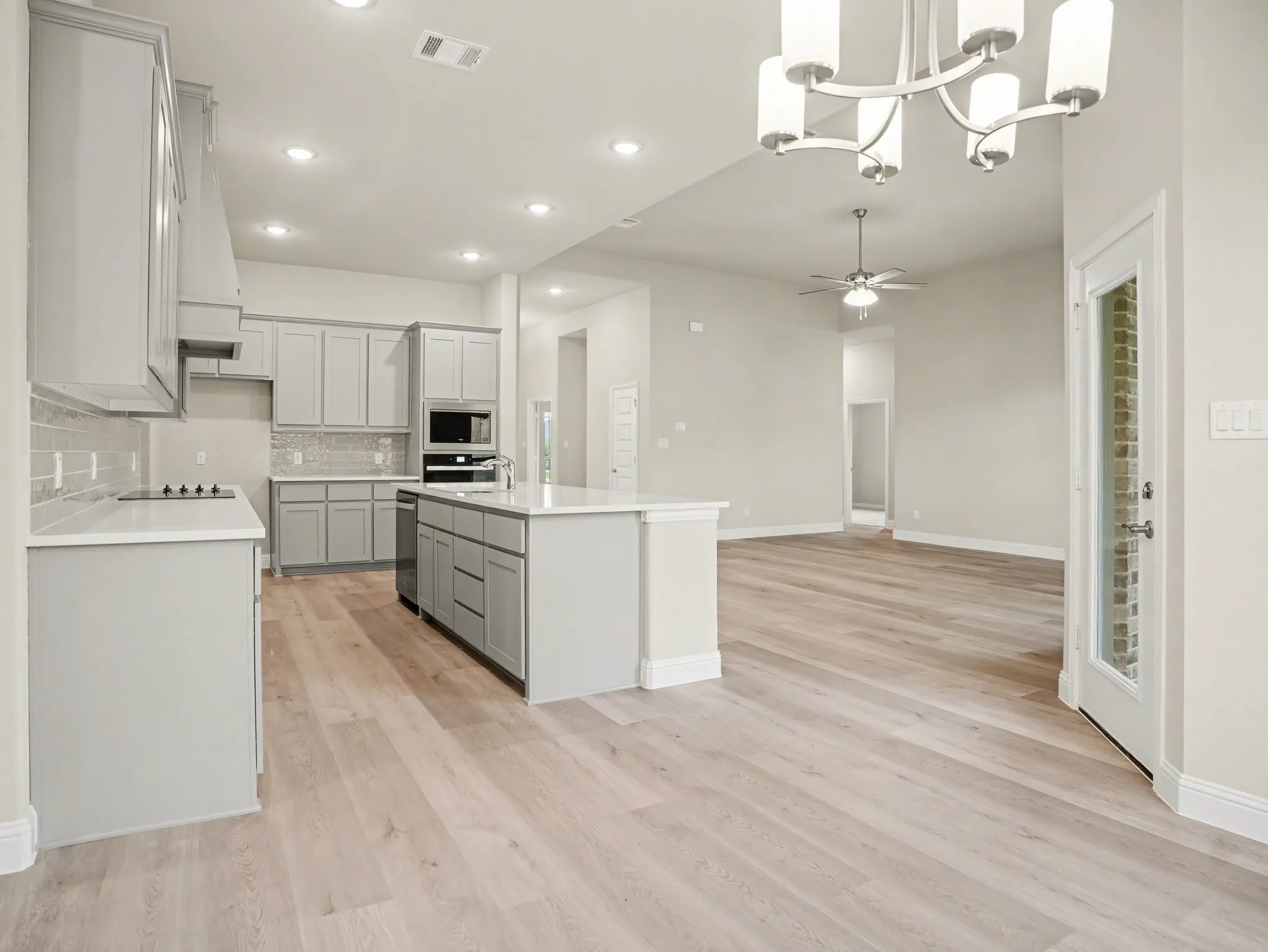 Modern kitchen featuring light gray cabinetry, a white countertop island, integrated microwave and oven, a white cooktop, and light wood-finish flooring