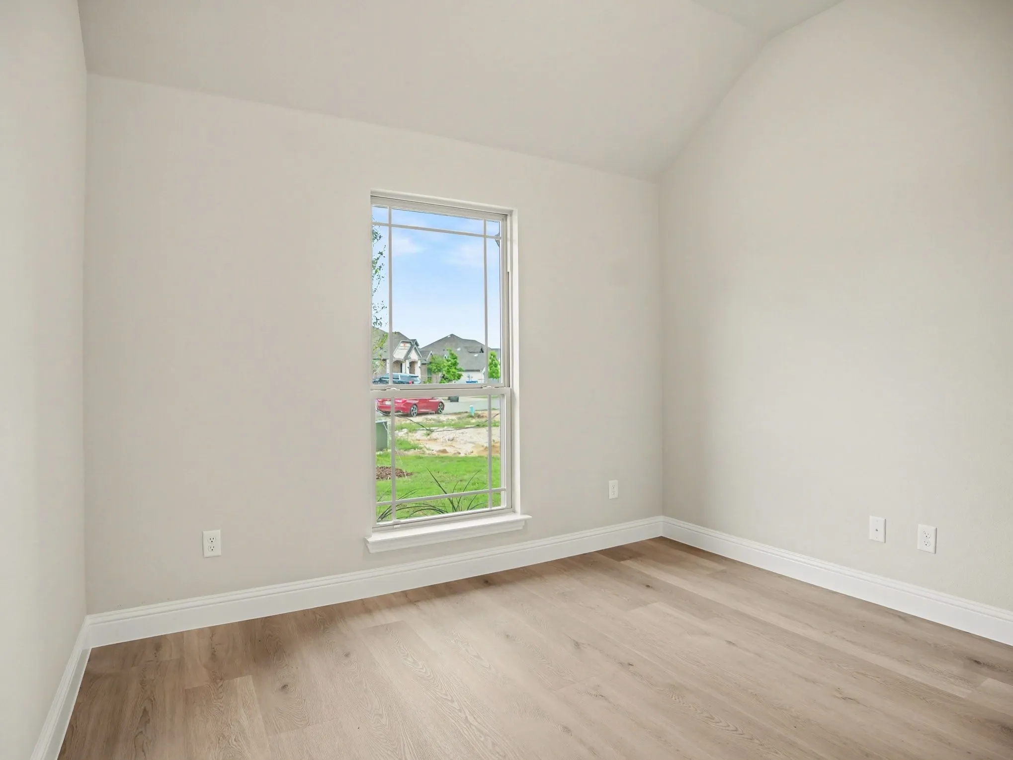 Vaulted ceiling room featuring light wood-finish flooring, a white trim window, and neutral wall paint