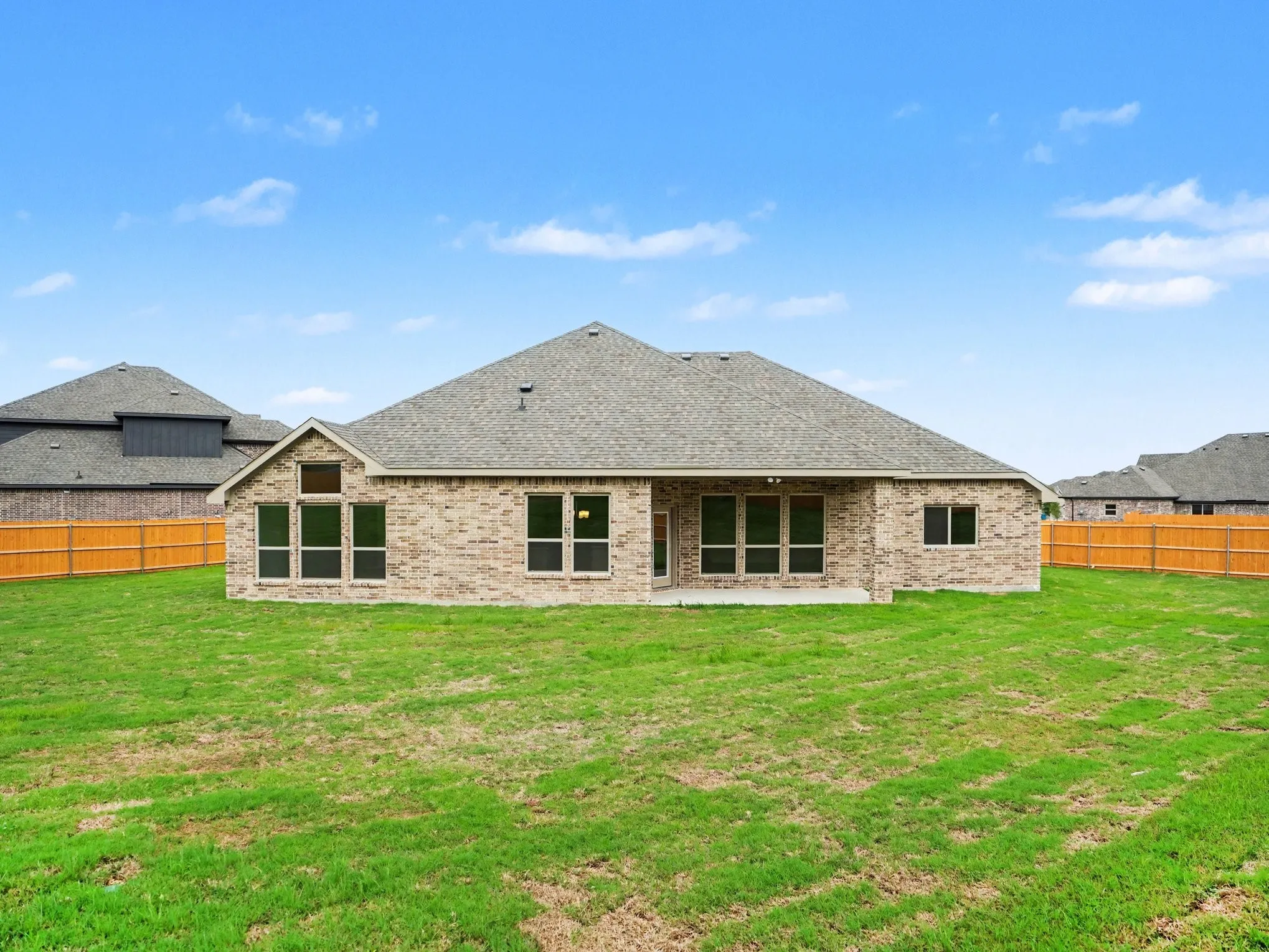 Expansive backyard with a manicured lawn, brick exterior, multiple windows, a private wood fence, and a covered patio