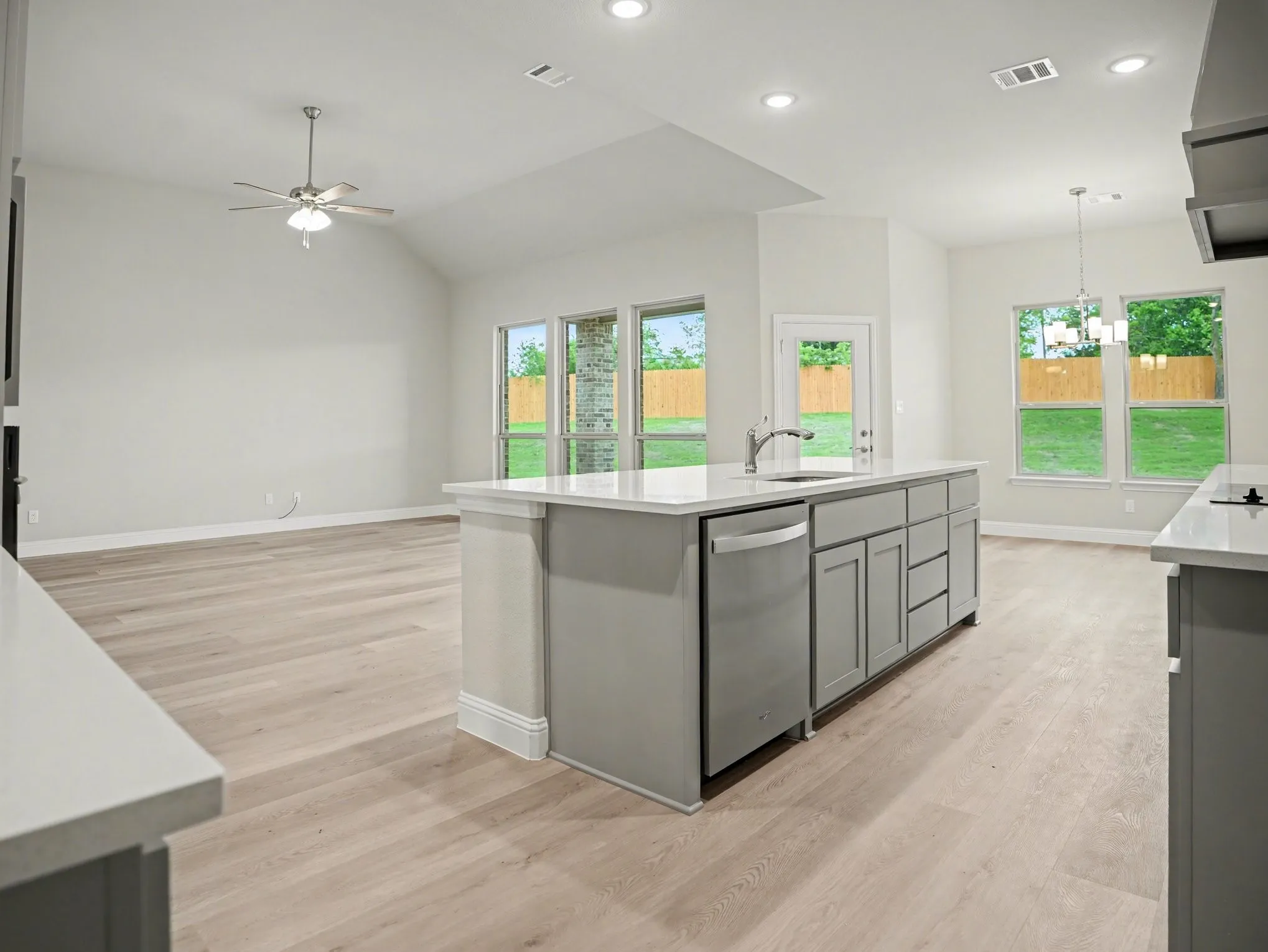 Kitchen island with light grey cabinetry, integrated sink, and stainless steel dishwasher