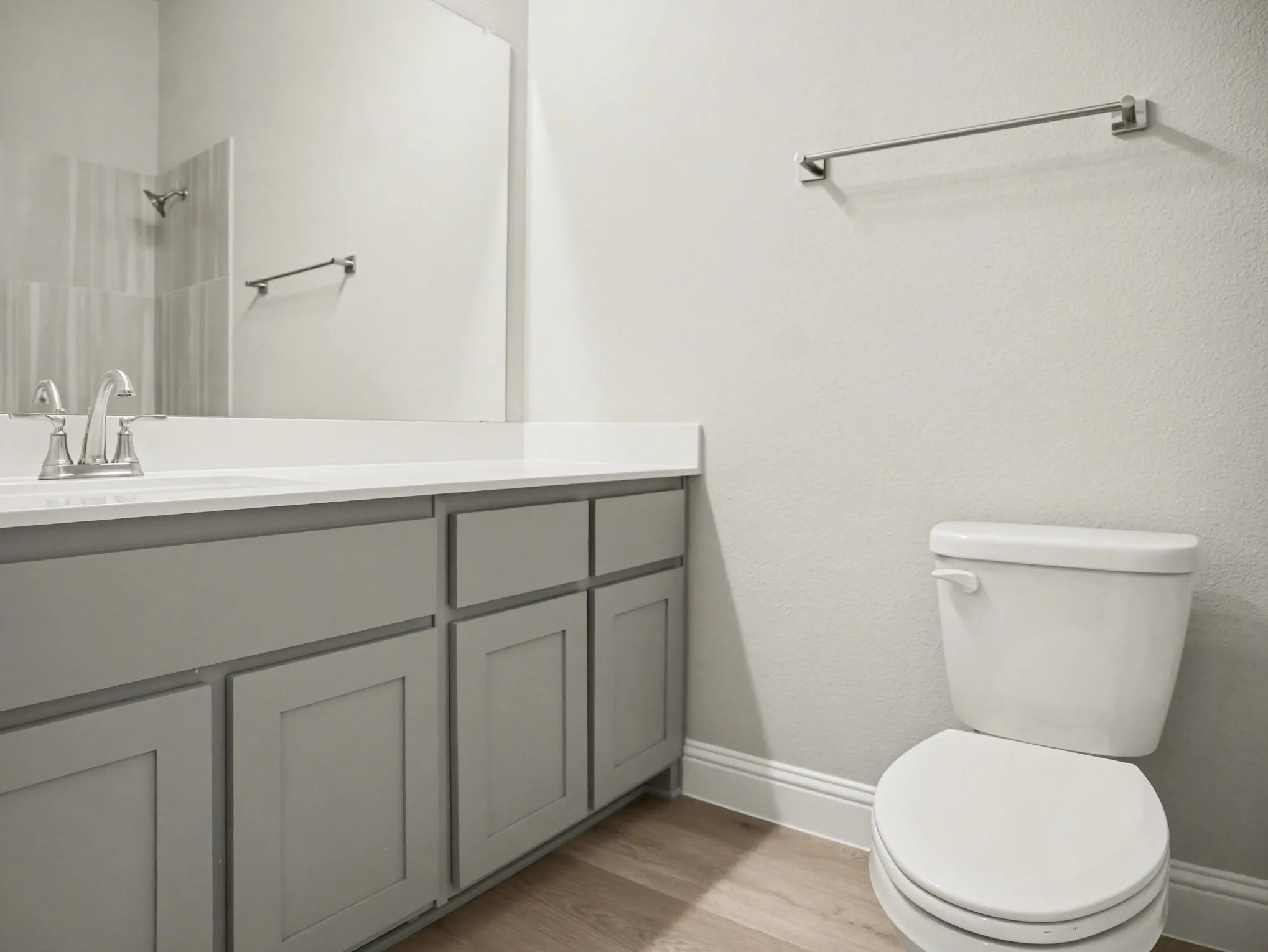 Bathroom featuring a white countertop with an integrated sink, brushed nickel faucet, large vanity mirror, light grey shaker-style cabinetry, and wood-finish flooring